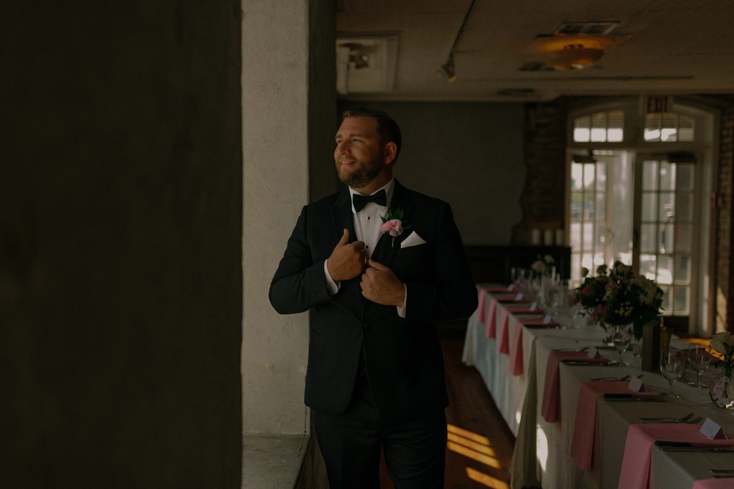 Man in a tuxedo standing by a window in a decorated dining room.