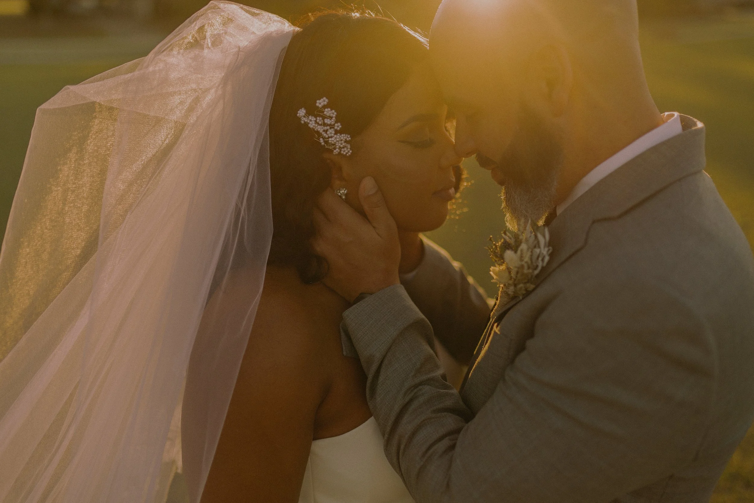 A bride and groom in an intimate embrace at sunset, with the bride wearing a veil and the groom in a suit.