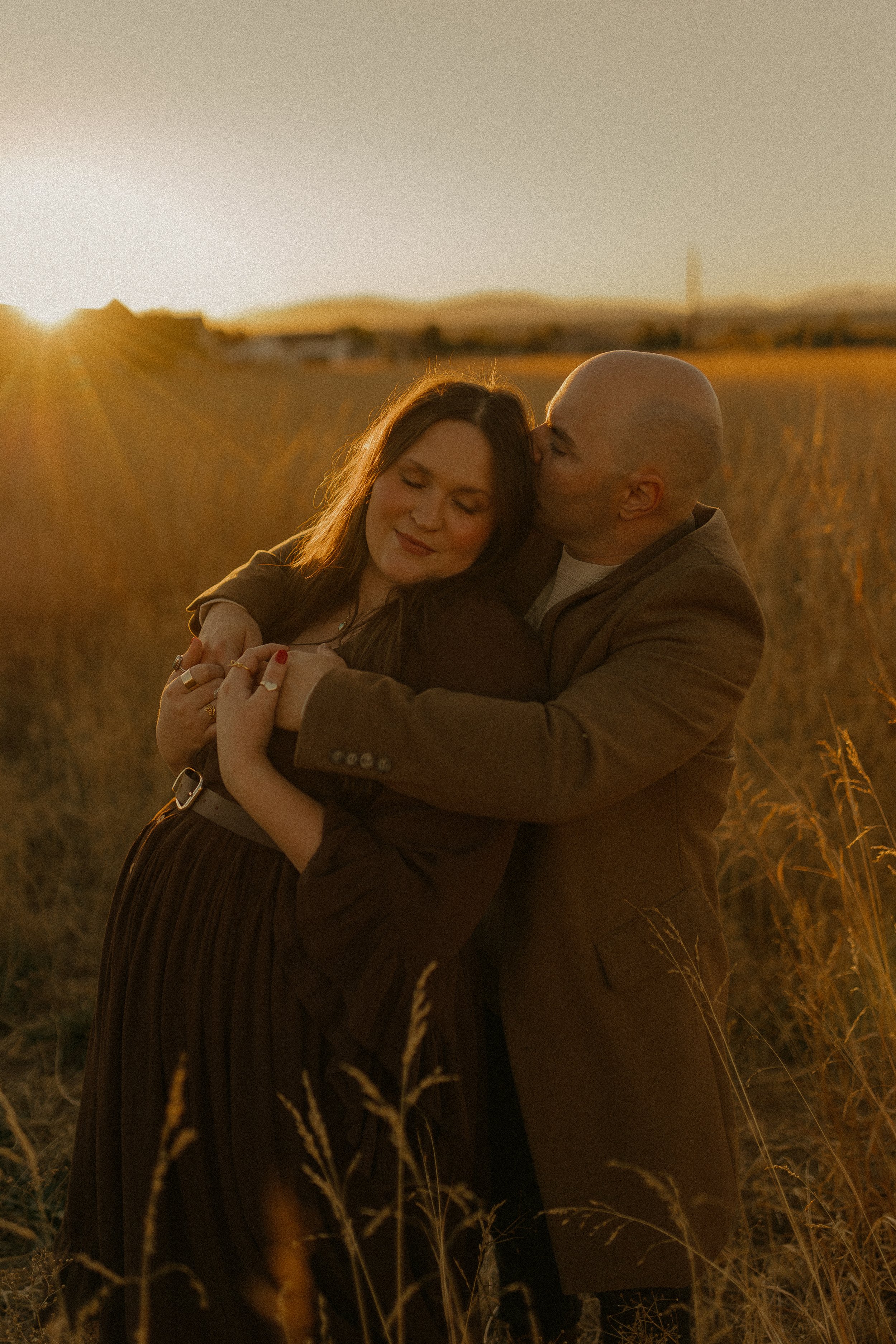 A couple embracing in a field at sunset, with golden light.