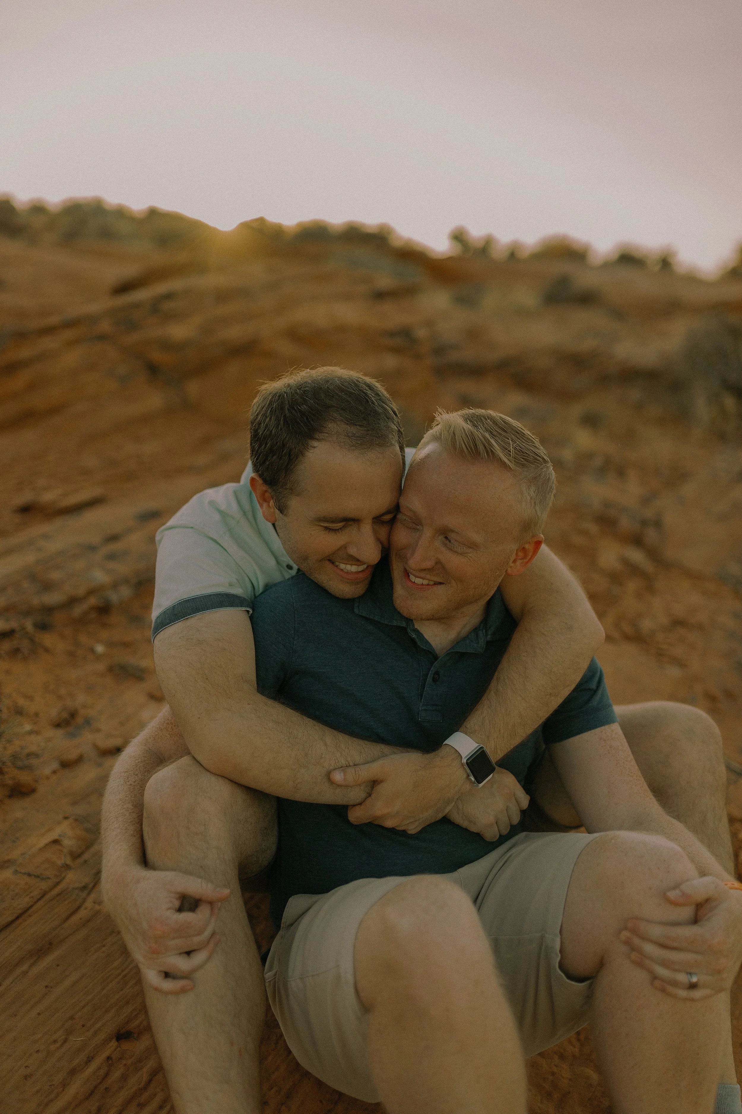 Two people hugging on a rocky landscape at sunset.