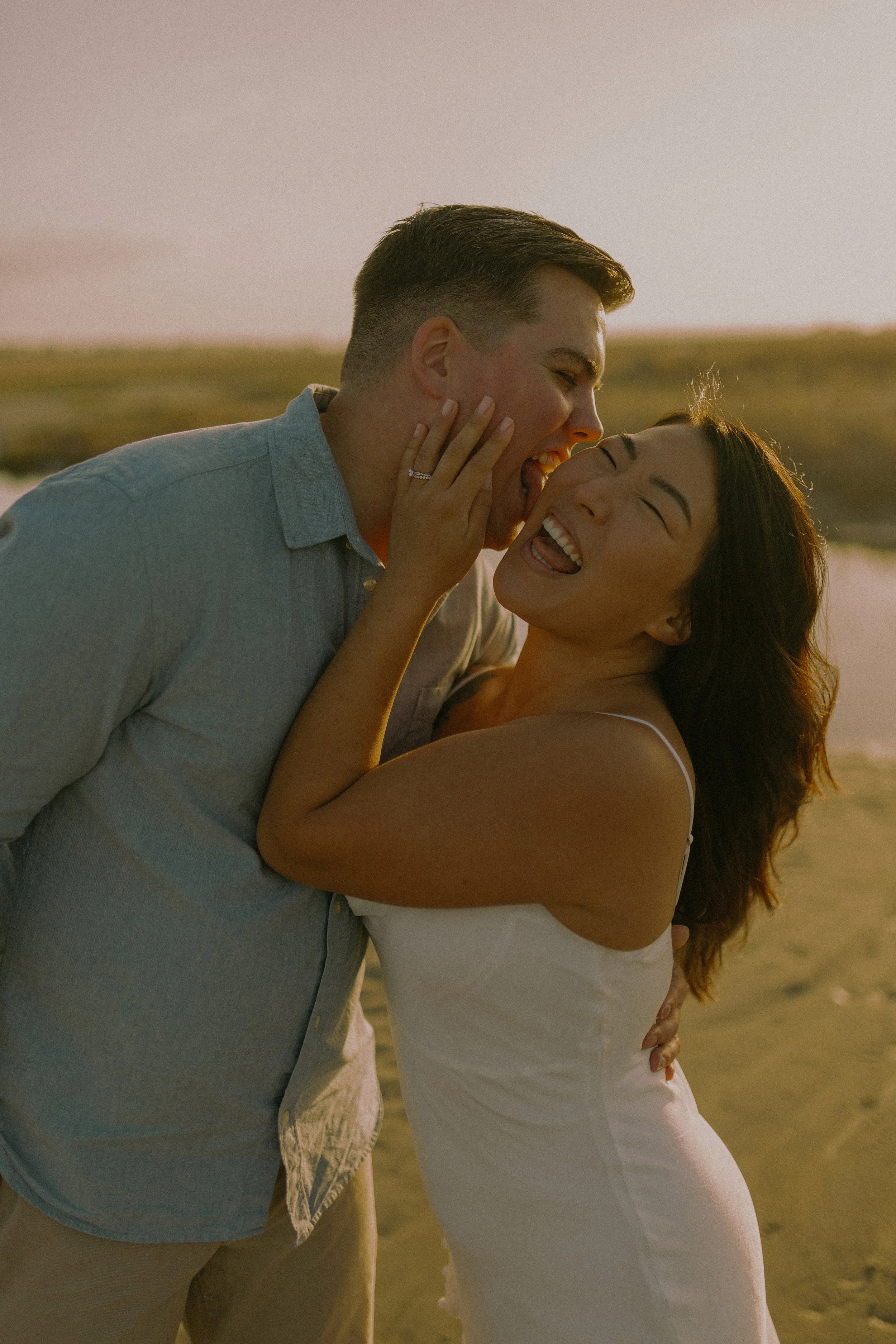 A couple laughing and embracing outdoors at sunset.