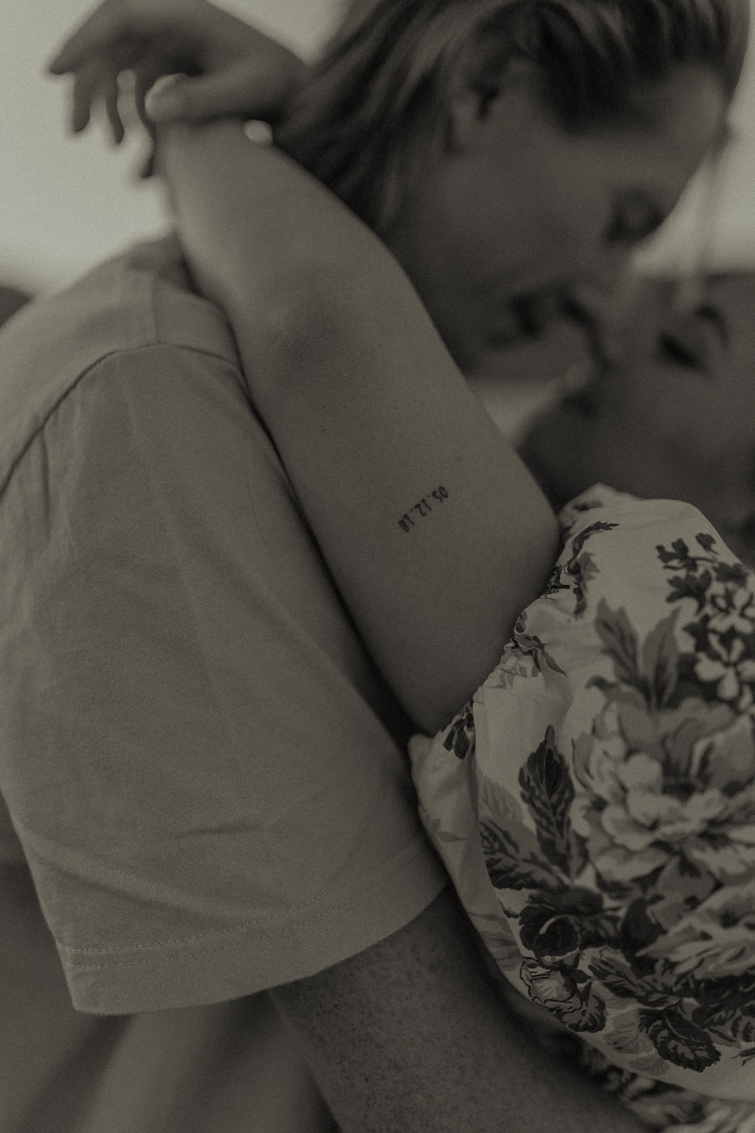 A close-up of two people embracing intimately, one person has a tattoo on their arm and is wearing a floral-patterned shirt.