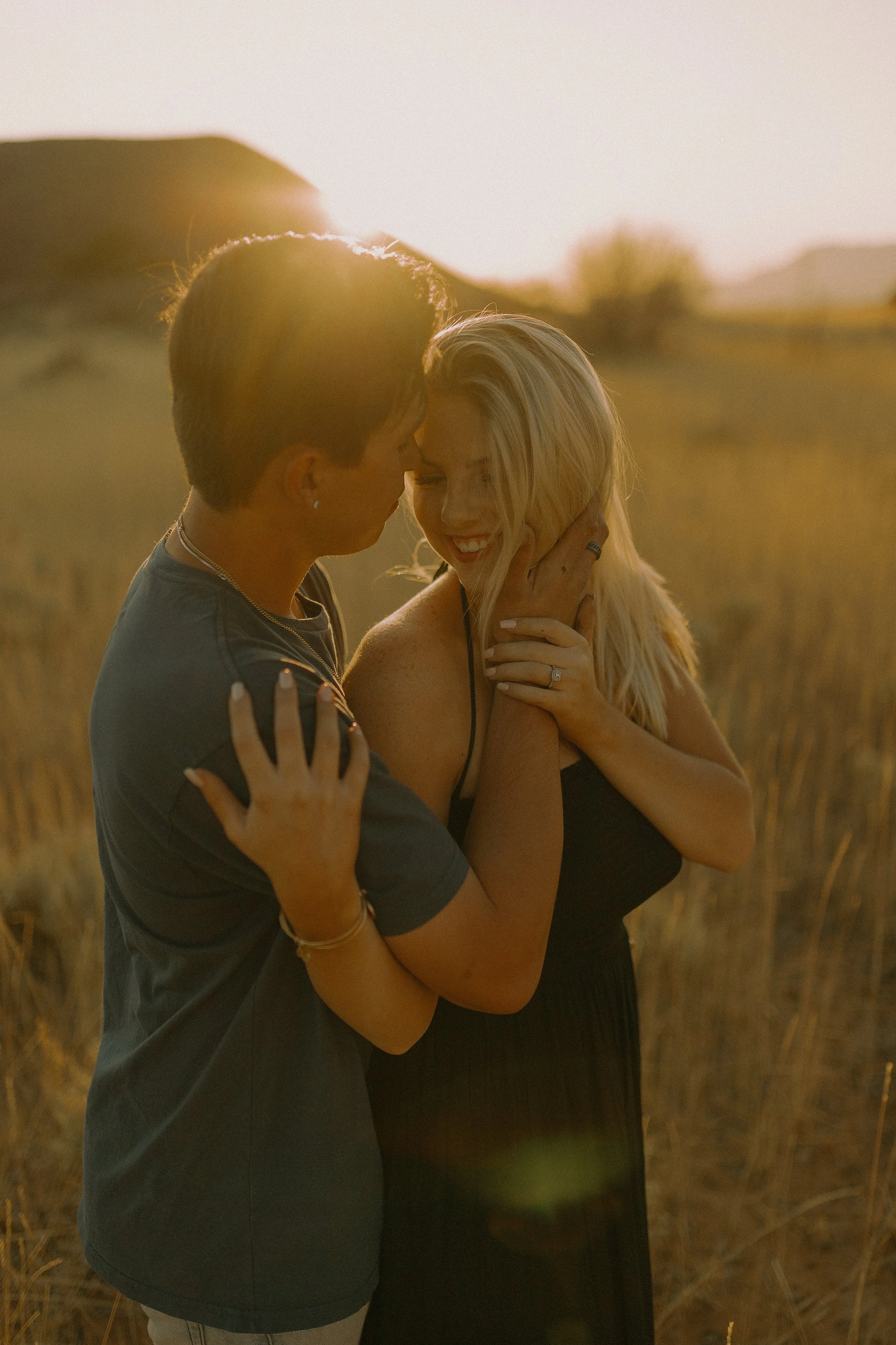 A couple embracing in a field at sunset, with warm sunlight creating a romantic glow.