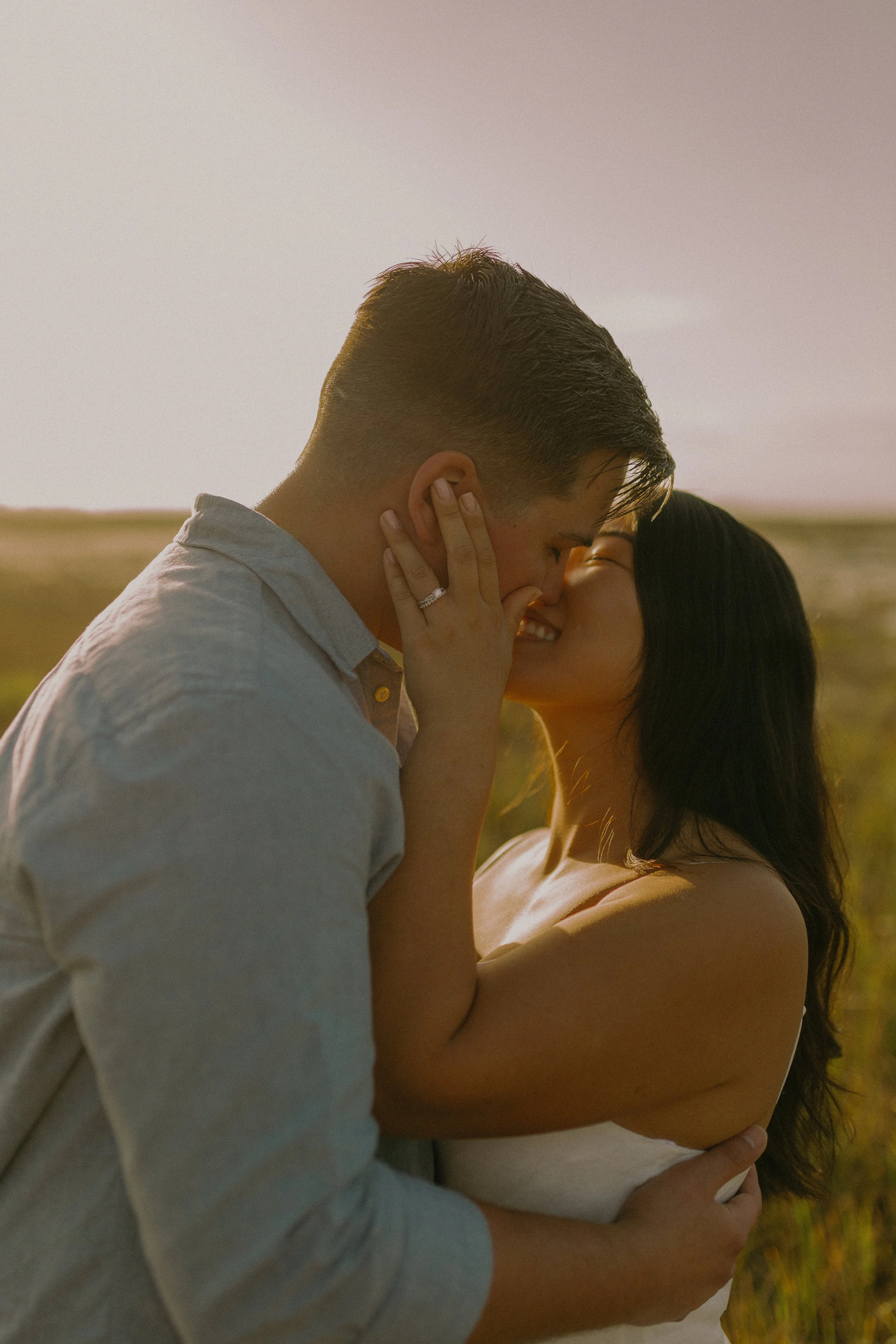 A romantic couple embraces and kisses in a sunlit field.