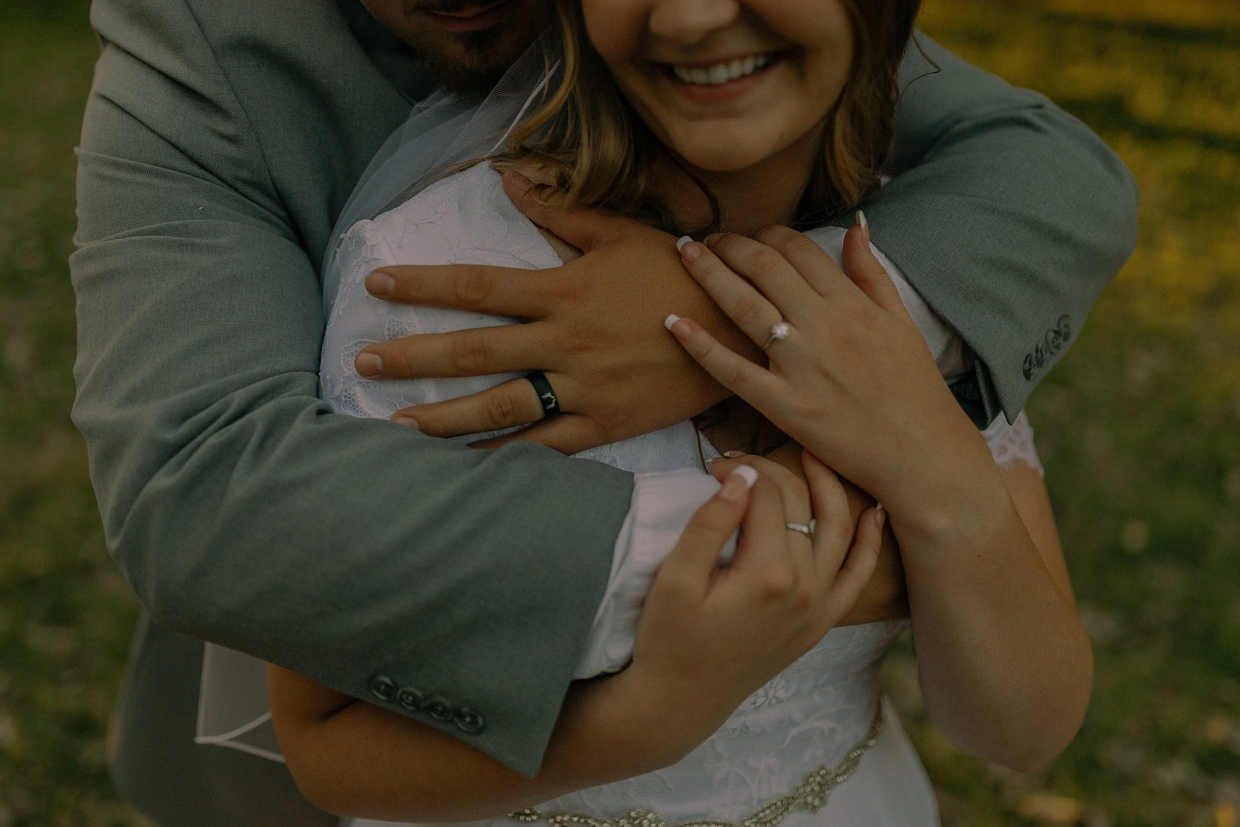 Close-up of a smiling couple embracing, showing hands with wedding rings.