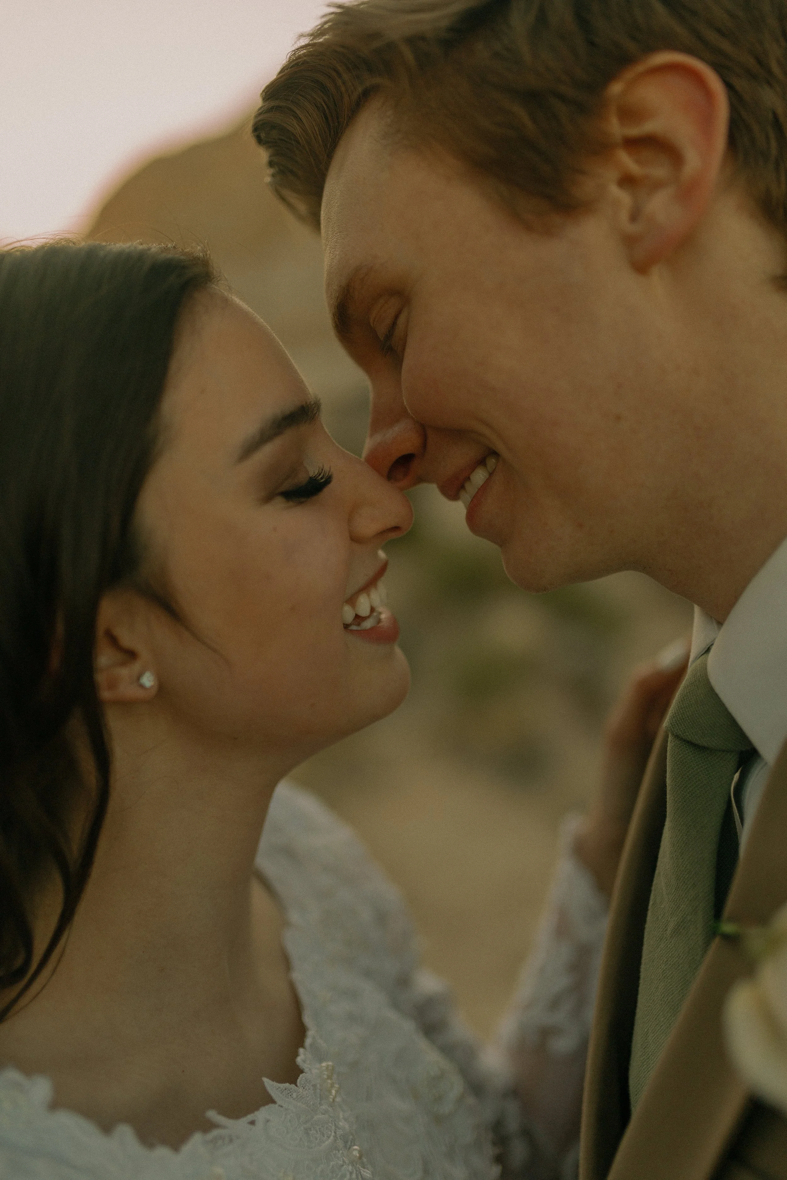 Close-up of a couple smiling and touching noses, wearing formal attire.