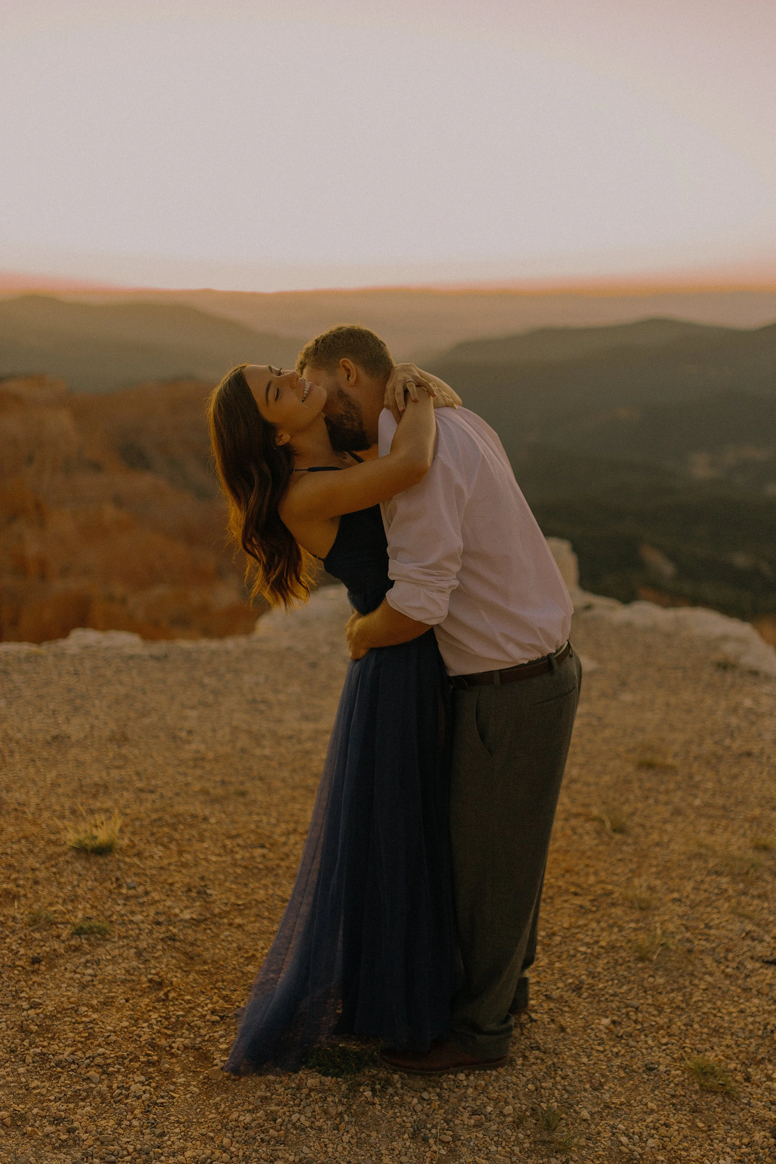 A couple embracing at sunset on a mountain with scenic views.