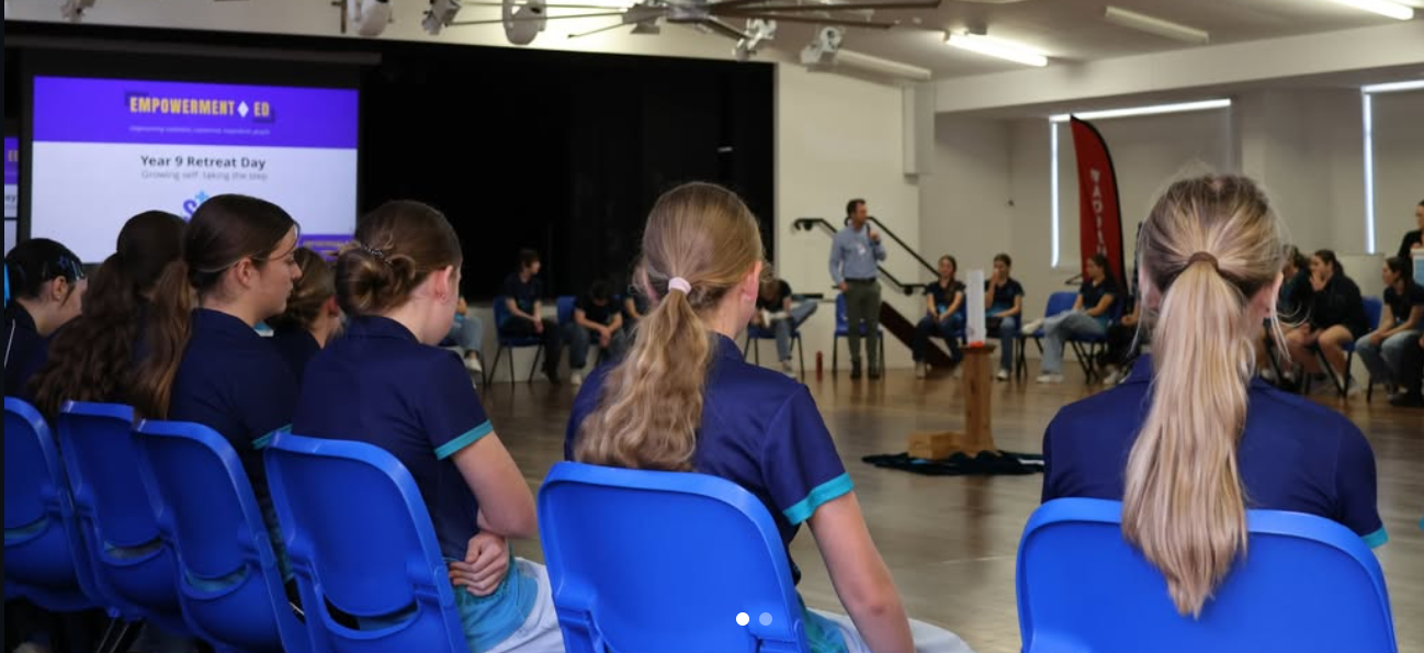 Students seated in groups inside a school gymnasium, attending an event or assembly.