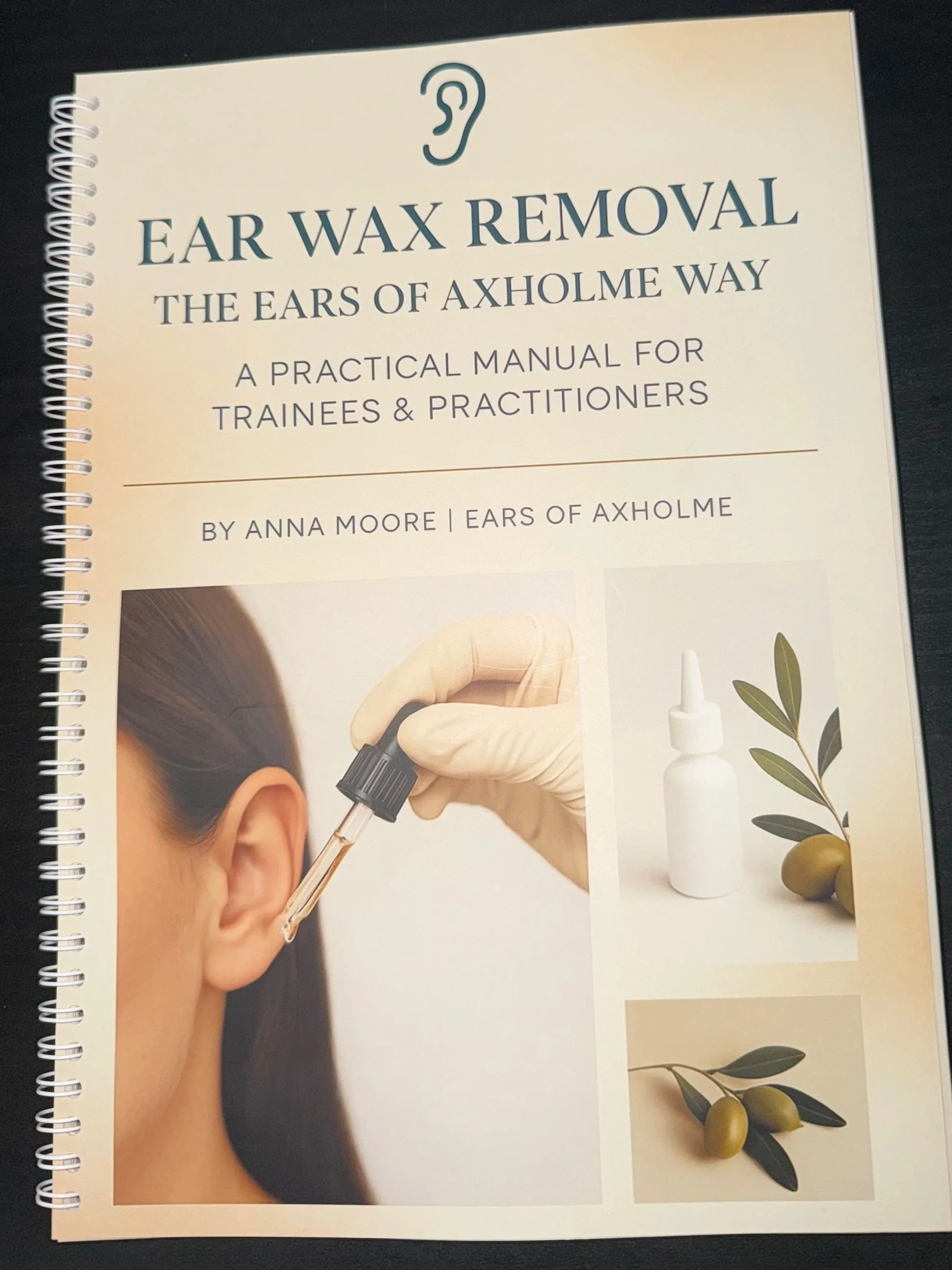 Book cover titled 'Ear Wax Removal: The Ears of Axholme Way, a Practical Manual for Trainees & Practitioners' by Anna Moore, featuring images of an ear, ear wax drops, and olives with leaves.