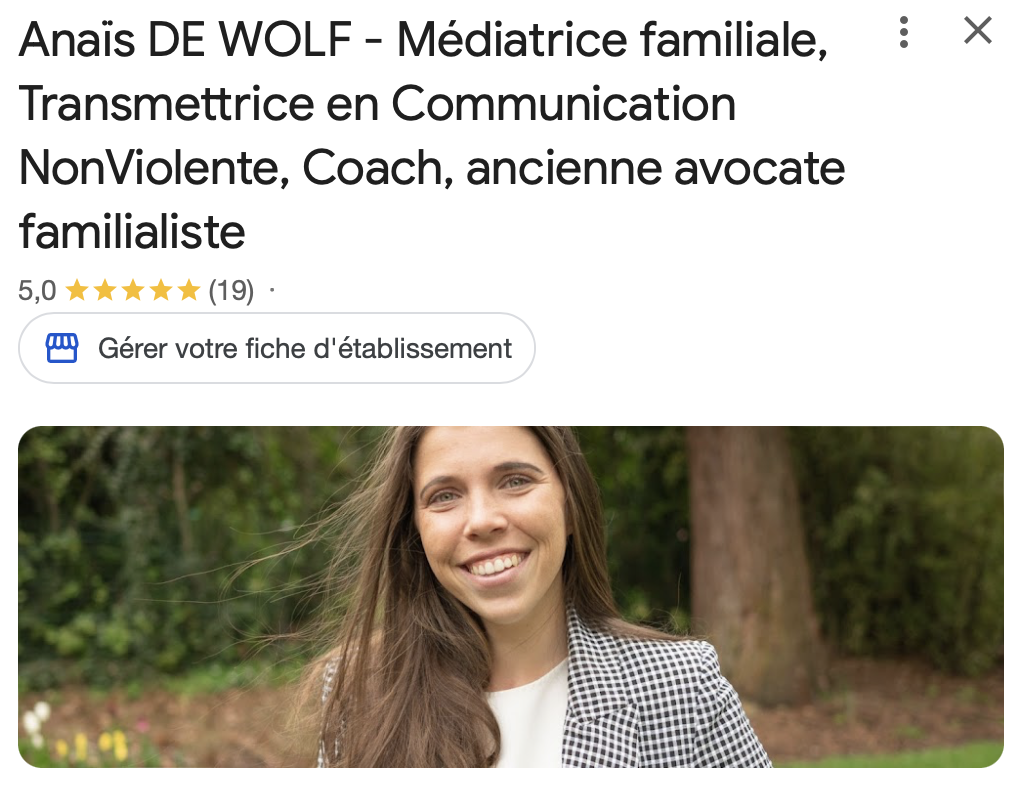 A woman with long brown hair and a checkered blazer smiling outdoors with trees in the background.