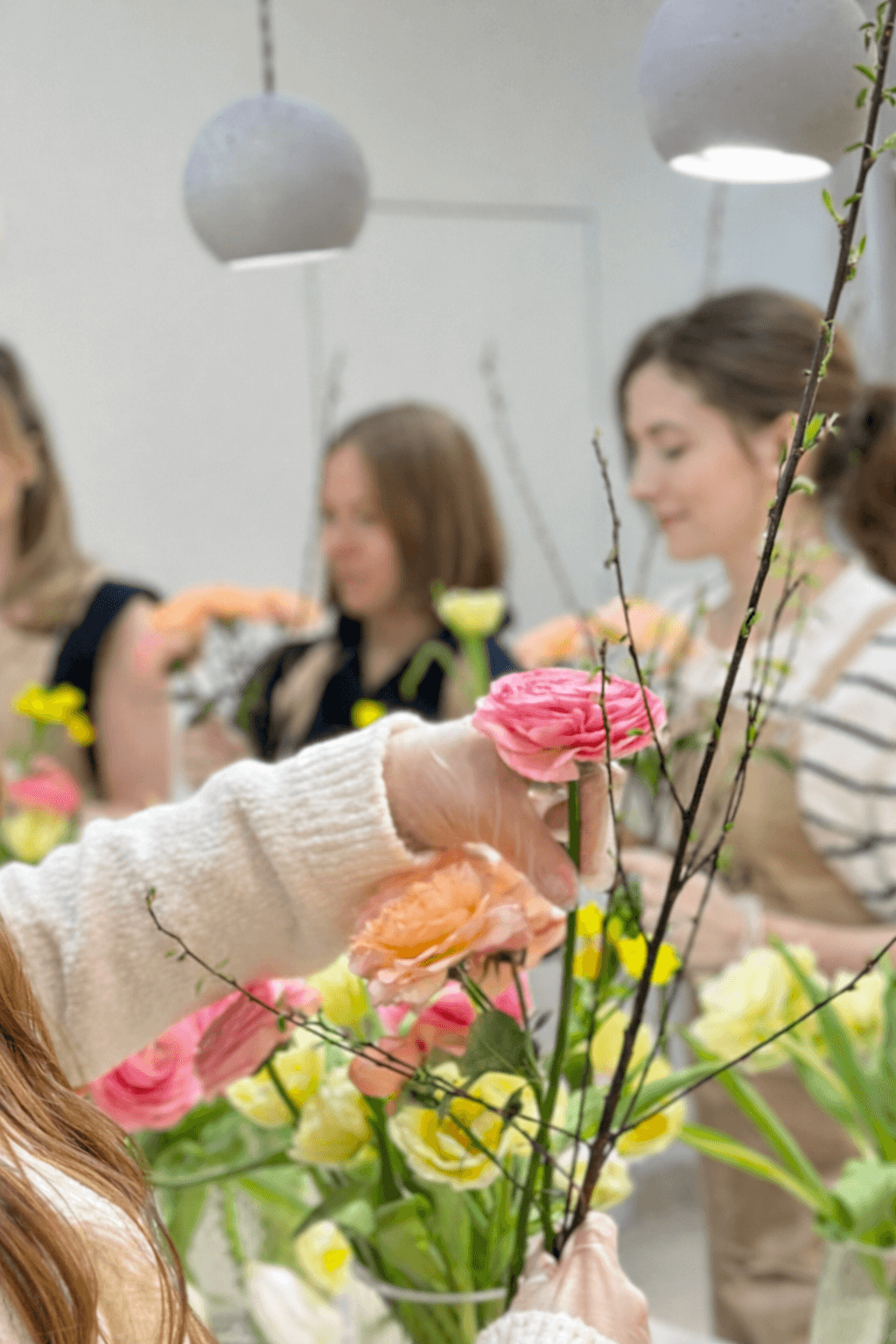 Młode kobiety układają bukiety z kwiatów w kolorach żółtym, różowym i brzoskwiniowym