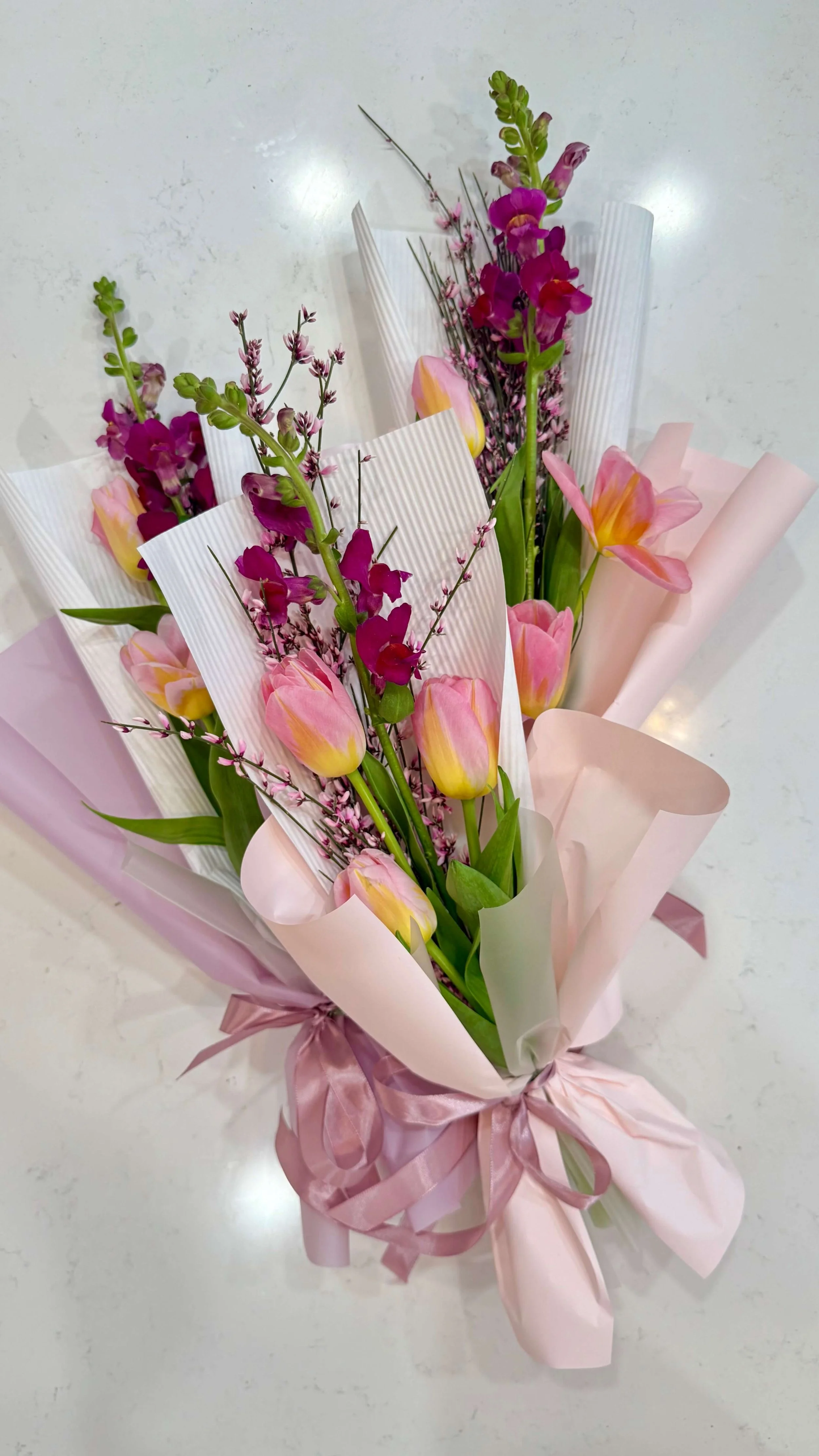 Niewielkie bukiety opakowane w papier ozdobny, tulipany i lwia paszcza w kolorach różu i fuksji.