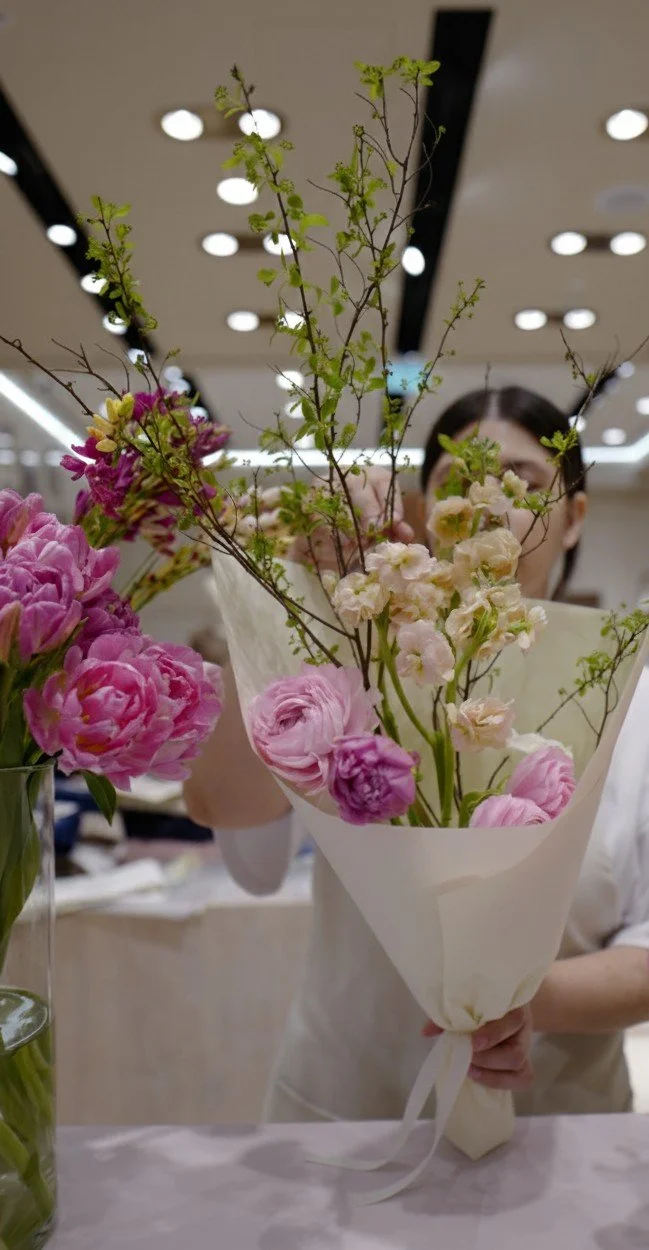 Osoba trzymająca bukiet różowych i białych kwiatów zawiniętych w biały papier pakowy.