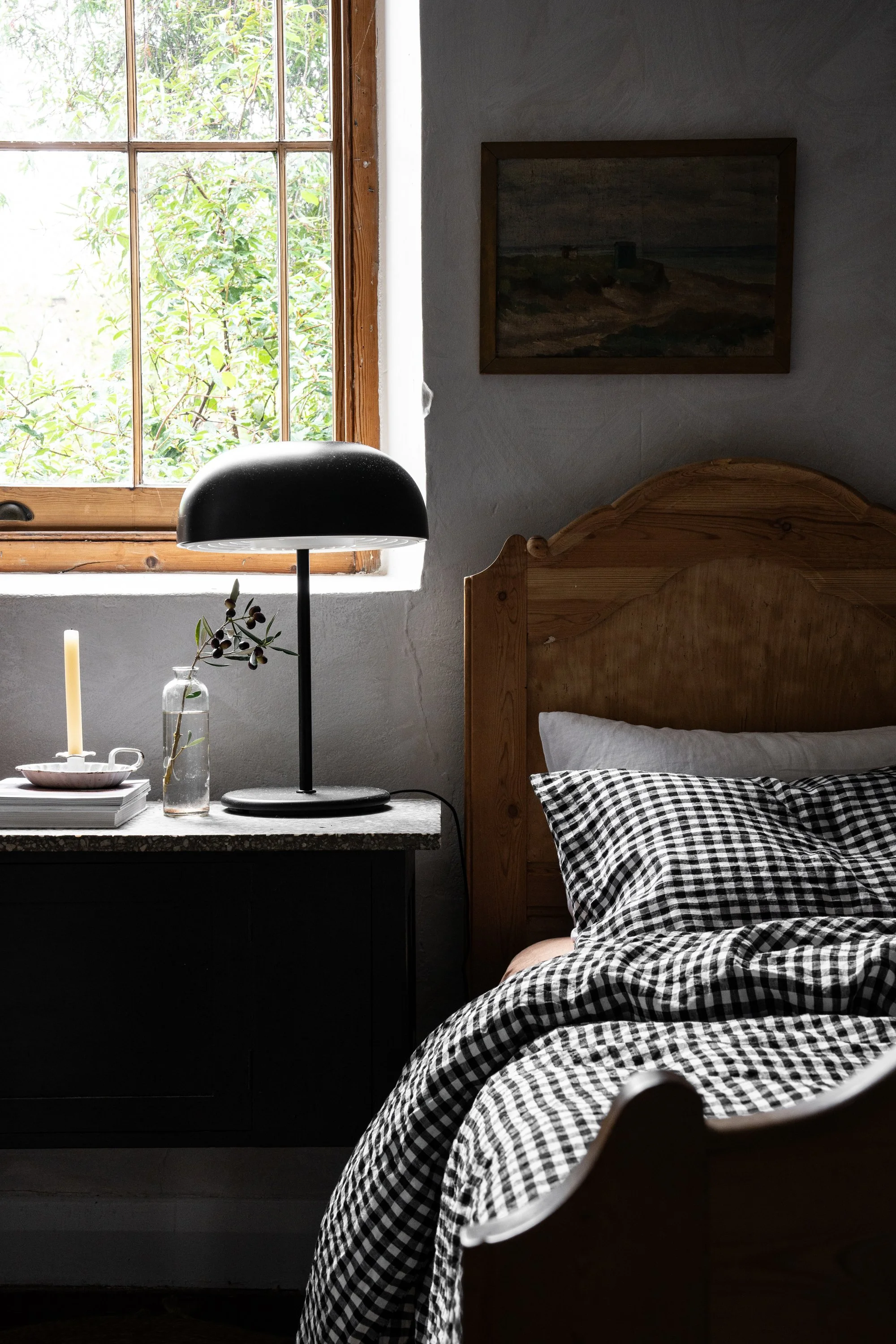 Moody bedroom interior with vintage timber bed, black lamp, gingham bedding and natural light