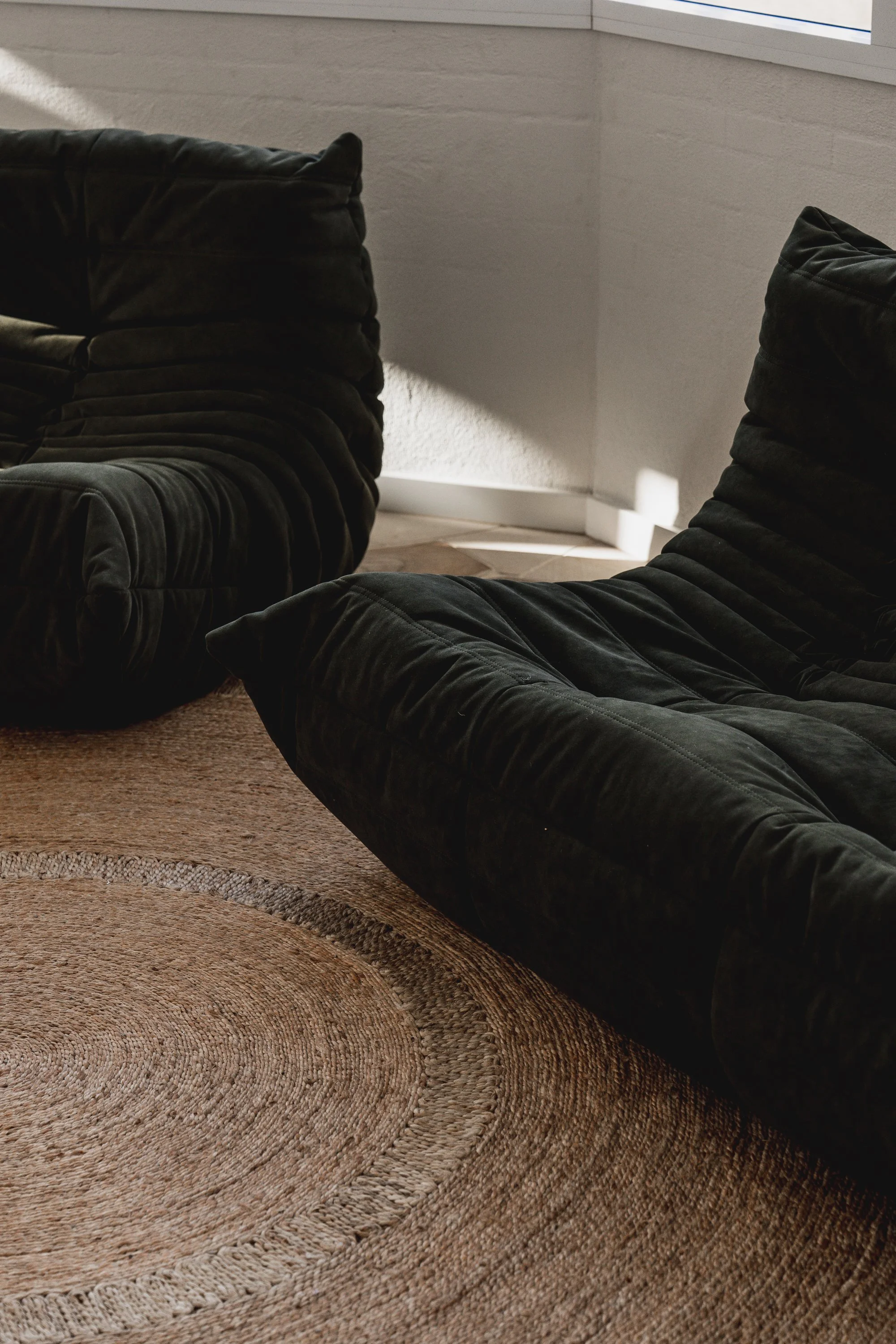 A person lounging on a brown, patterned, circular area rug, with black velvet cushions and a textured wall in the background.