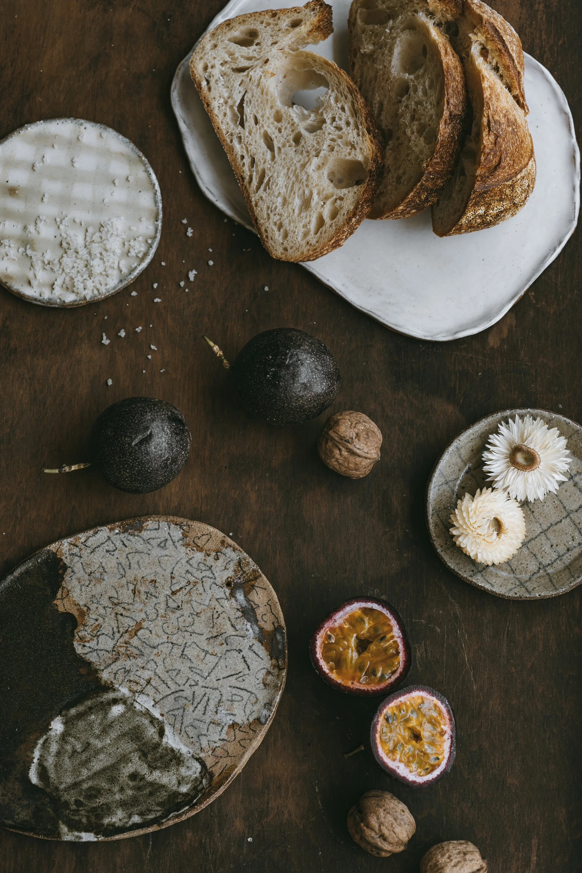 Editorial still life of artisan bread, ceramics, fruit and flowers on a textured timber table