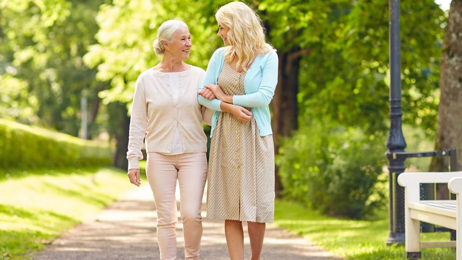 An elderly woman and her caregiver enjoying a walk in a lush park, demonstrating active lifestyle support for seniors.