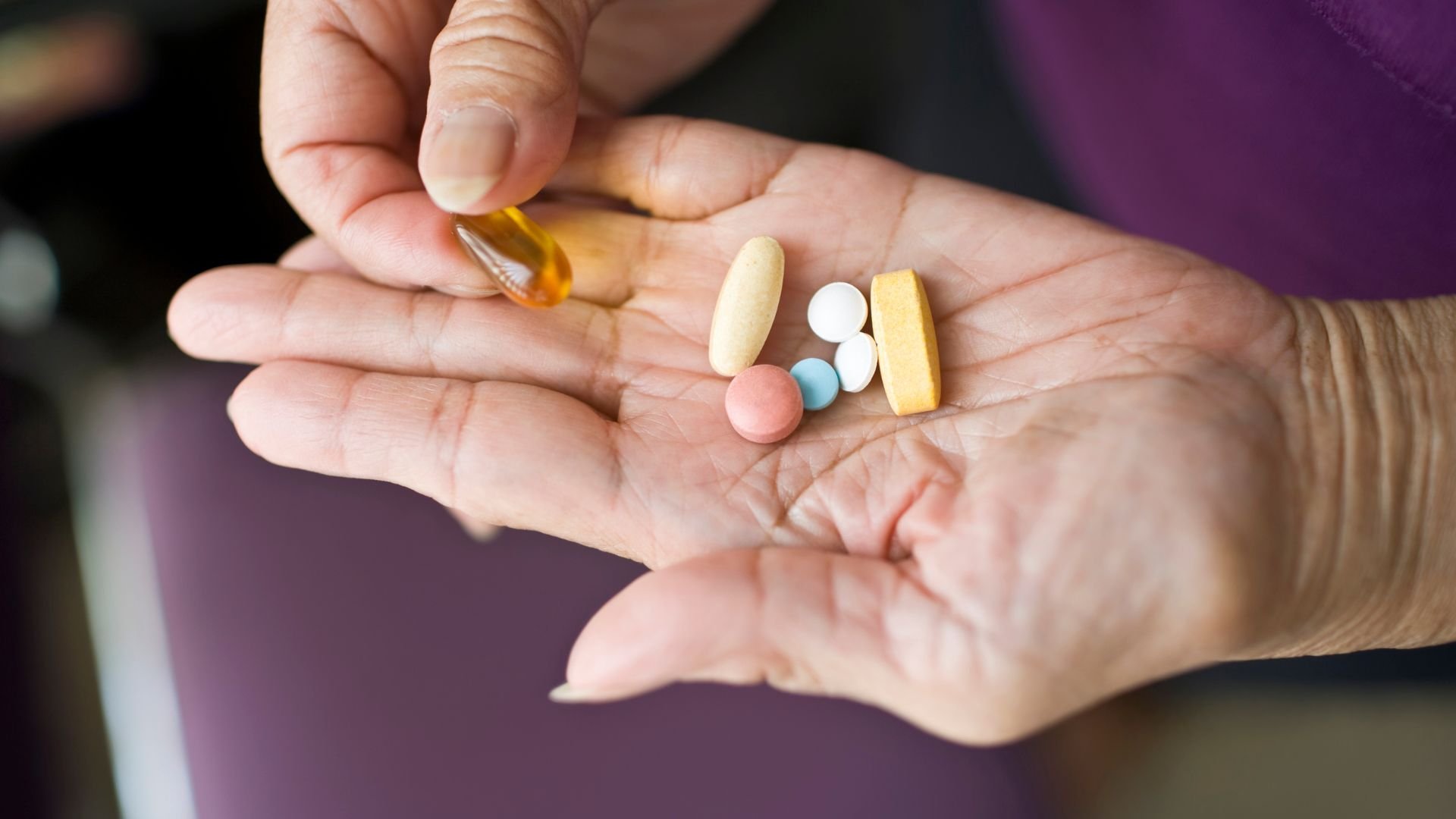 An elderly person gently holds a variety of colorful pills in their open hand, highlighting the importance of medication management for seniors.