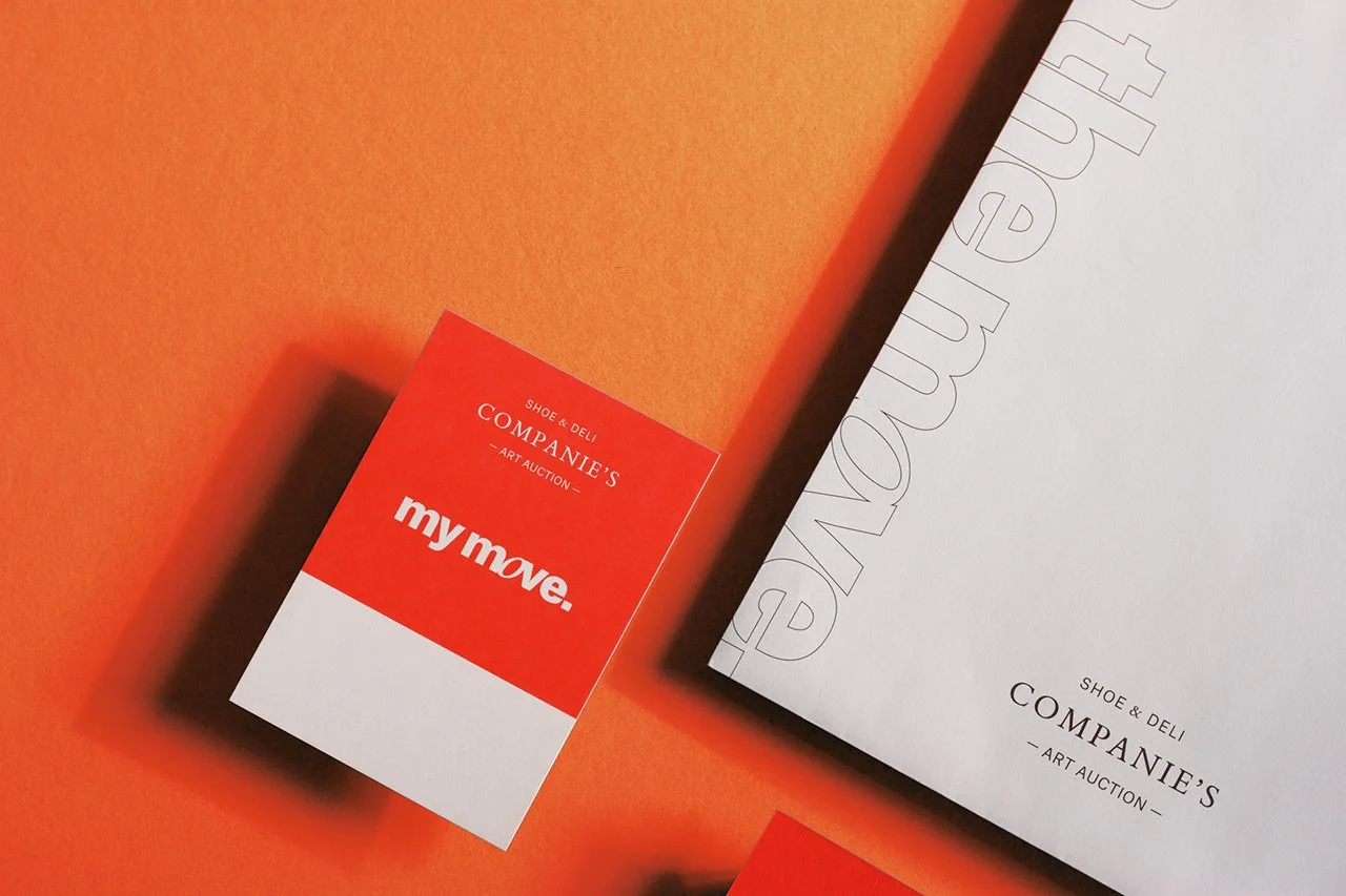 Ein rotes und weißes Auktionskärtchen mit dem Text "my move." und einem größeren white Auktionskatalog mit dem Text "SHOE & DELI COMPANIE'S ART AUCTION" auf einem orangefarbenen Hintergrund.