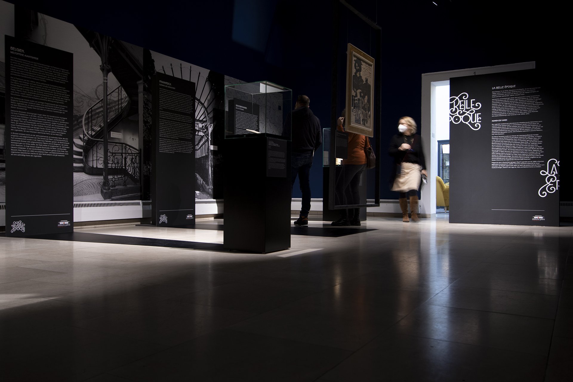Ausstellung in einem Museum mit mehreren Besuchern, die die Infotafeln und Kunstwerke betrachten.