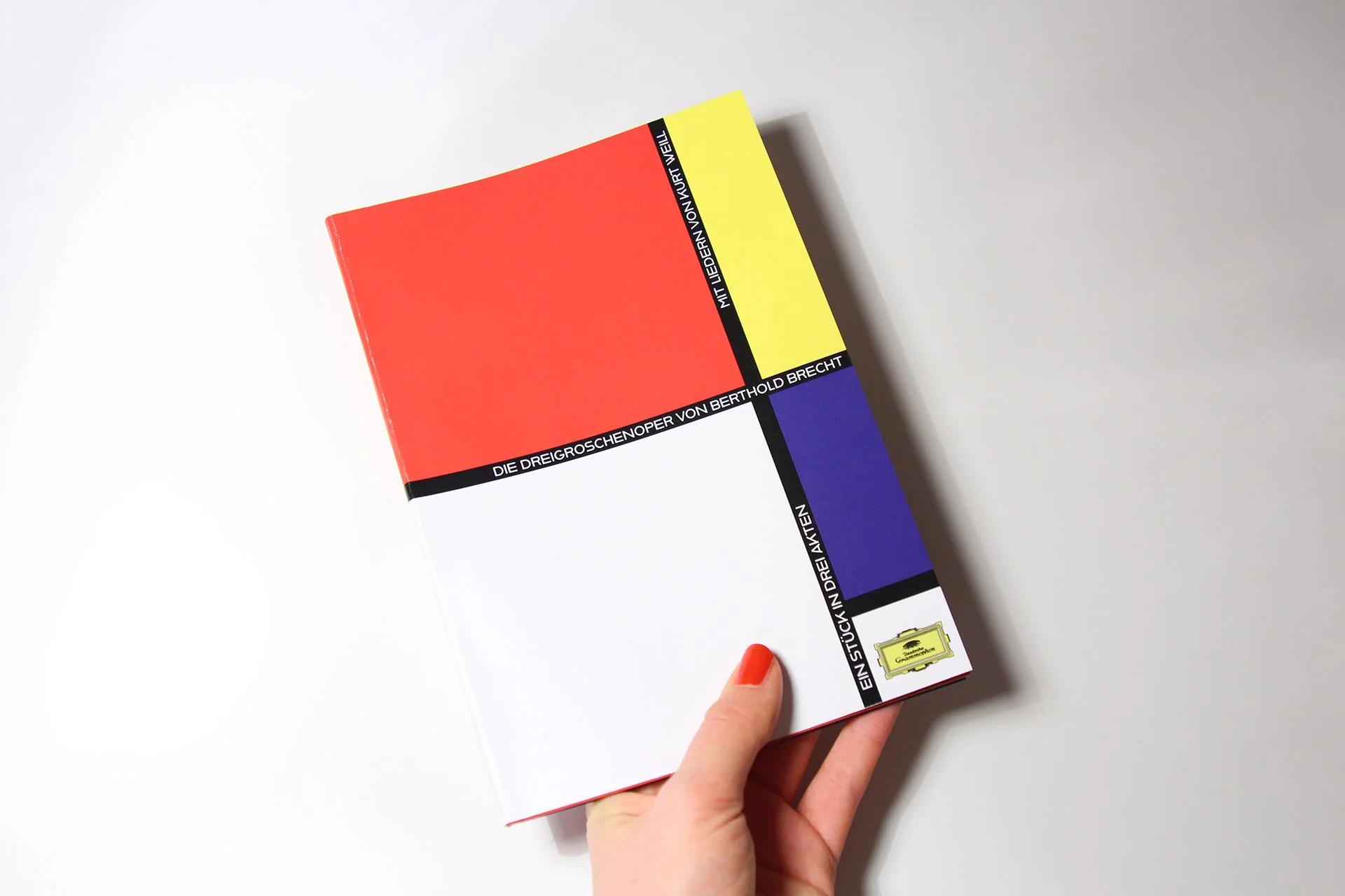 Das Buch mit farbigem Cover in den Farben rot, gelb, schwarz, weiß und blau, das von einer Hand gehalten wird, liegt auf einem weißen Hintergrund.