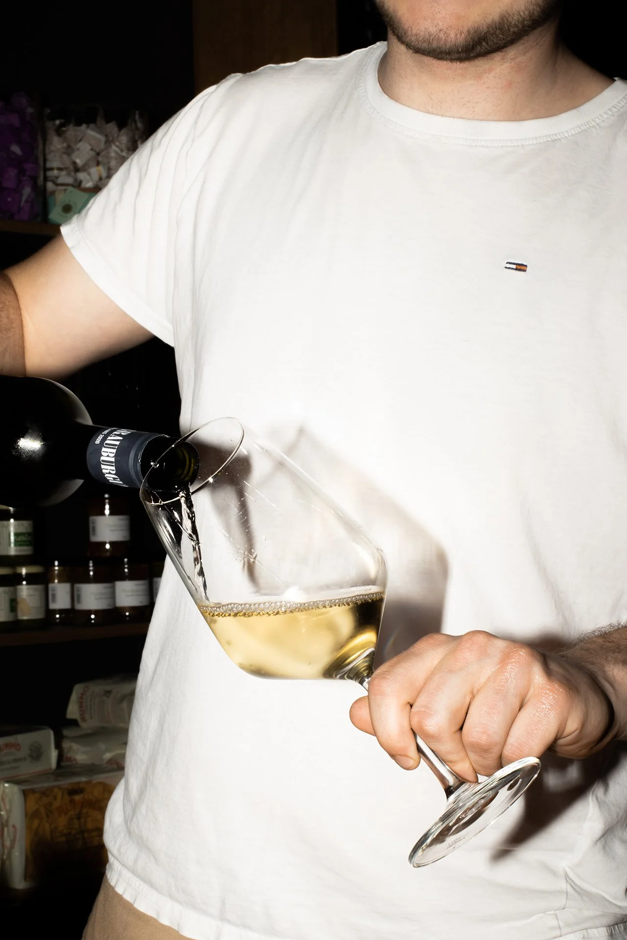 Ein Mann in weißem T-Shirt gießt weißen Wein in ein Weinglas.