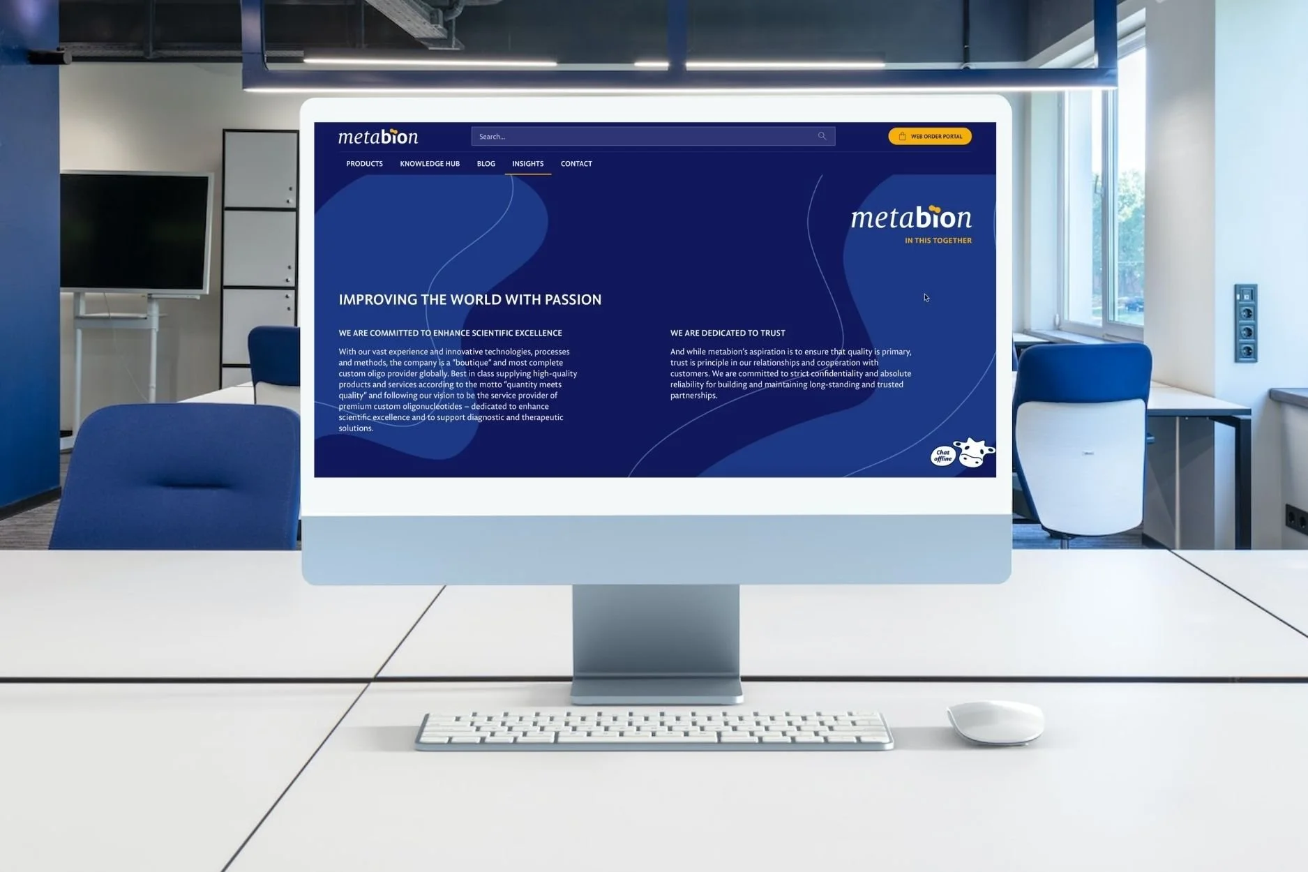 Computerbildschirm zeigt Webseite 'metabion' mit Texten und Navigation, im Büro mit weißen Tisch, Tastatur und Maus, im Hintergrund Bürostühle, Fenster und Stromleitungen.