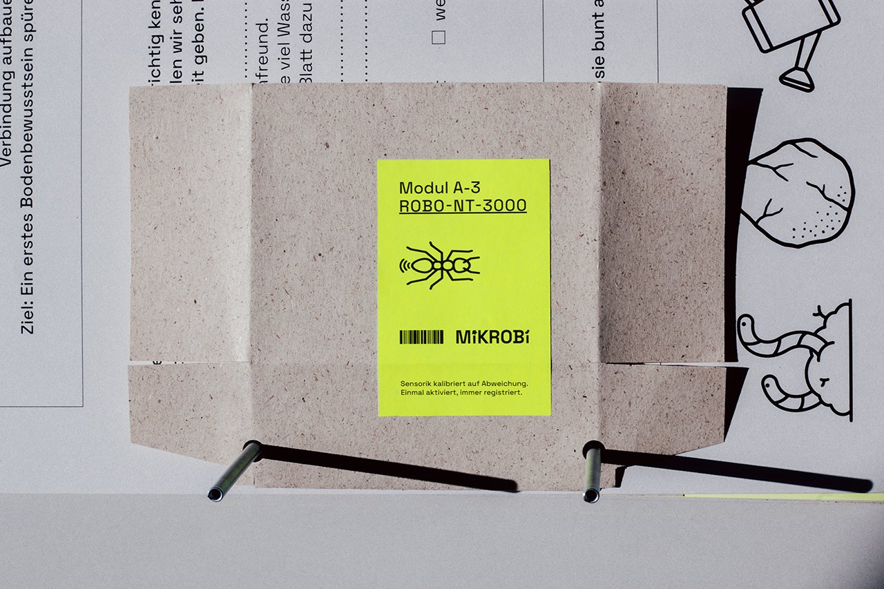 Ein rechteckiges, graues Gerät mit einem leuchtend gelben Etikett, das einen Code, die Begriffe 'Modul A-3' und 'ROBO-NT-3000', sowie eine Barcode-Abbildung.