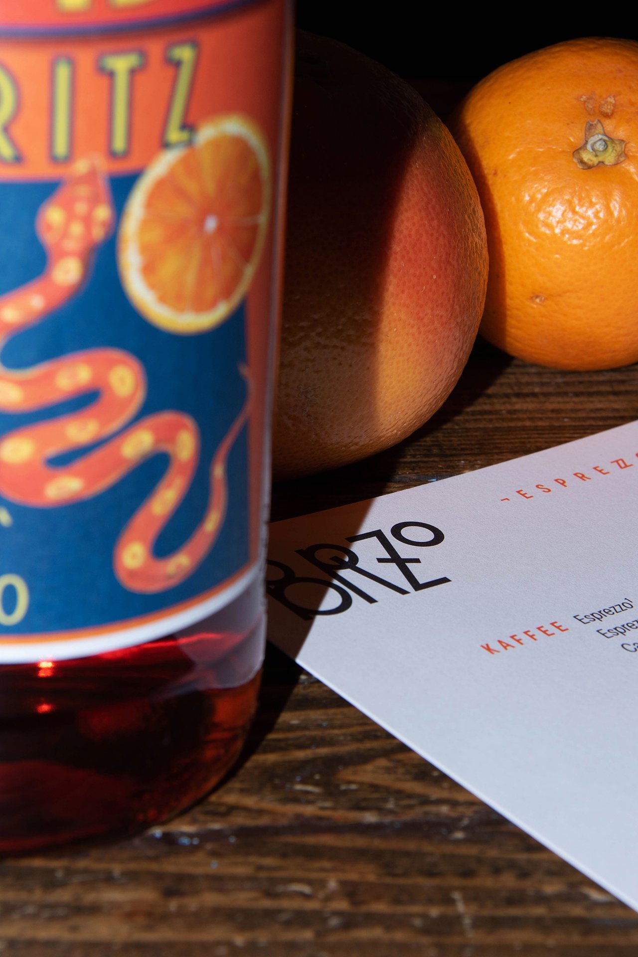 Ein Glas mit Orangensaft, zwei Orangen und eine Speisekarte auf einem Holztisch.