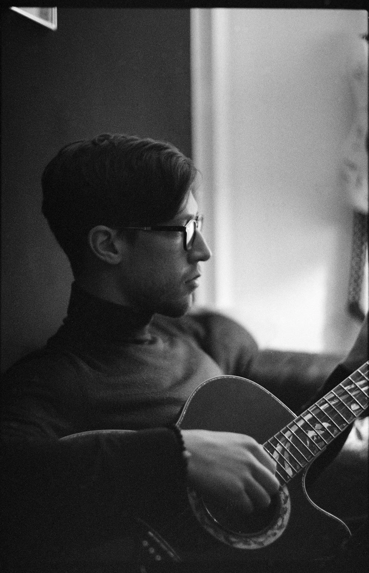 Schwarz-Weiß-Foto eines jungen Mannes mit Brille, der Gitarre spielt.