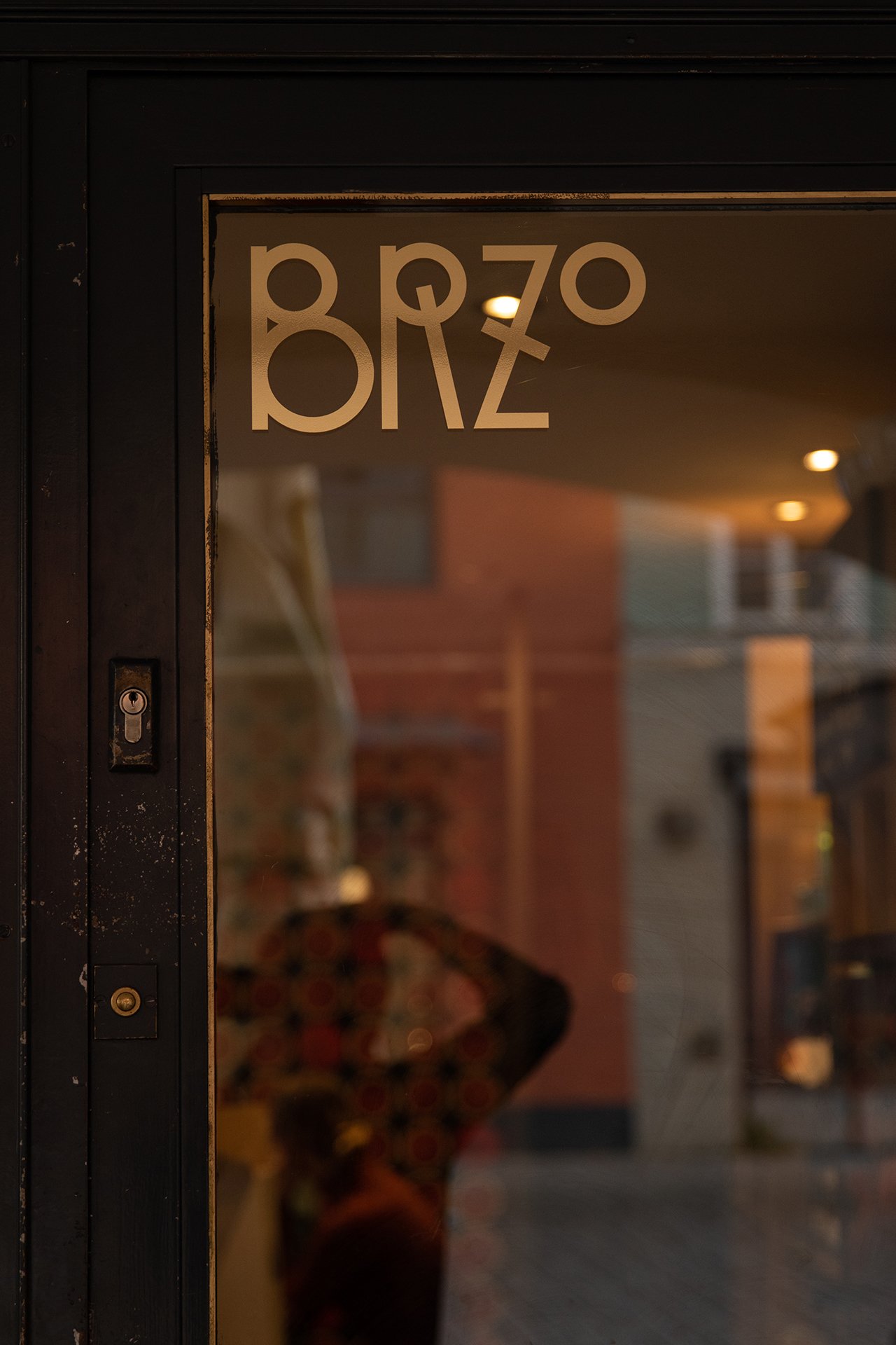 Blick durch eine Glastür auf das Innere eines Cafés oder Ladens, mit einem Menschen, der einen Regenschirm trägt, im Hintergrund.