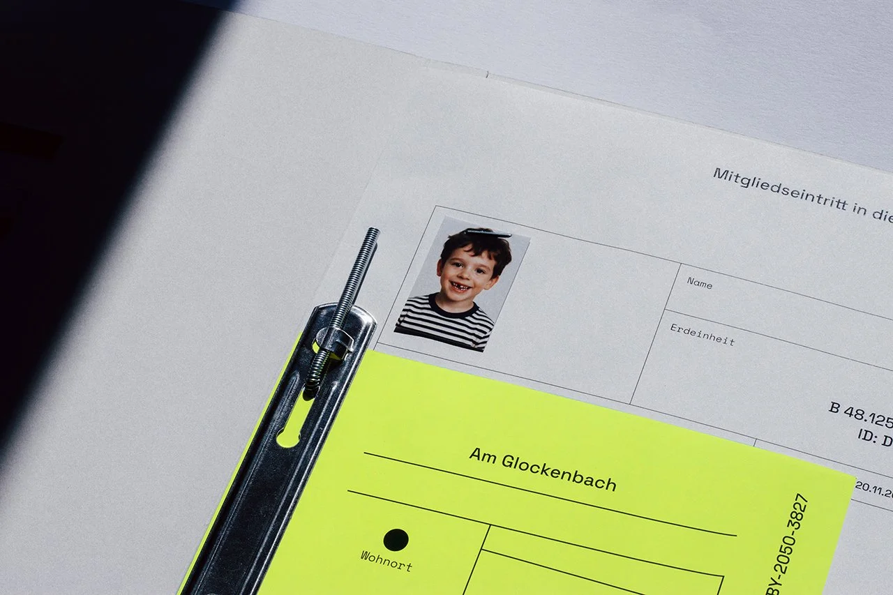Ein Mitgliedsausweis mit einem Kinderfoto, einem gelben Dokument mit der Aufschrift "Am Glockenbach" und einem schwarzen Punkt, sowie ein geöffneter Brief.
