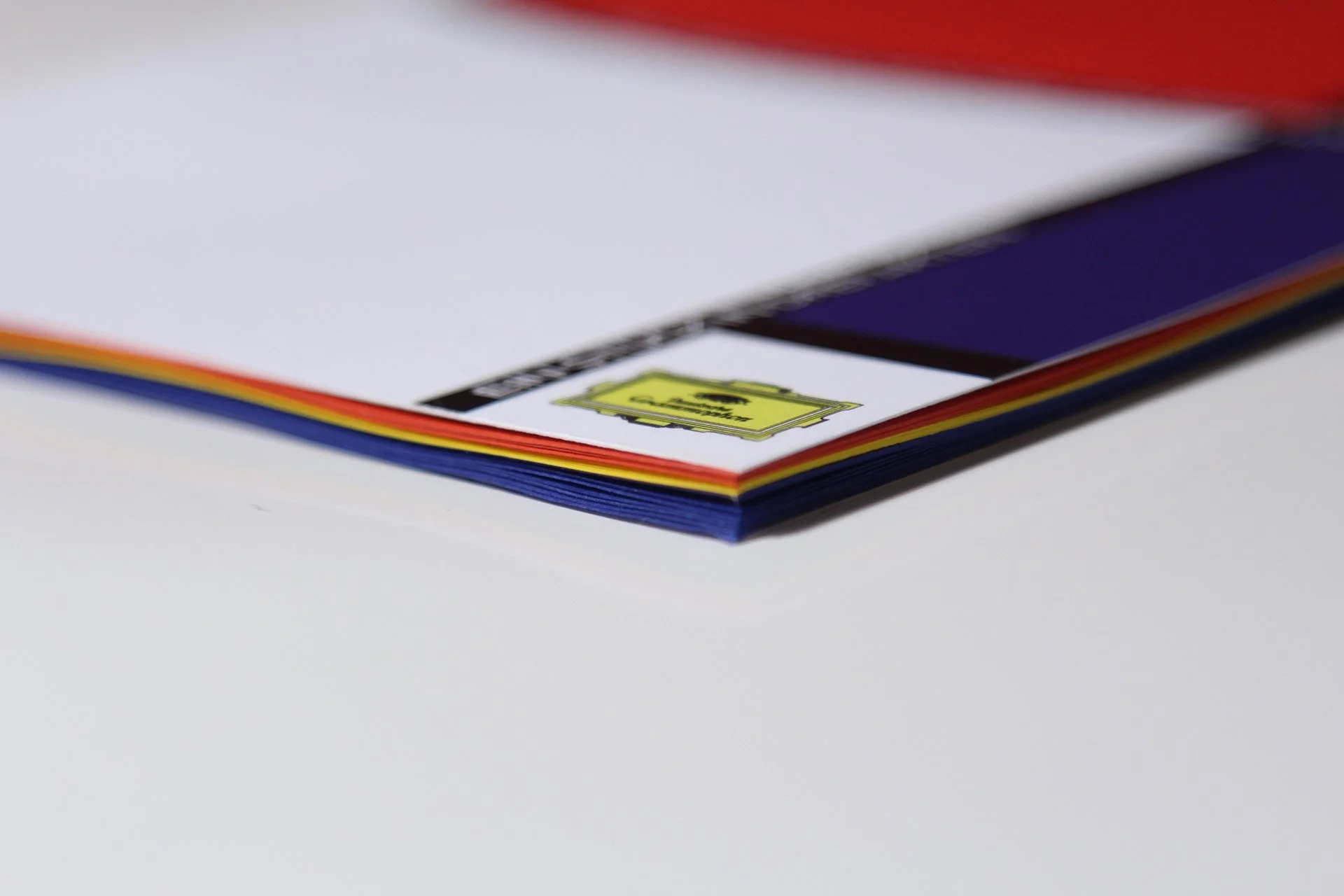 Ein Blätterstapel mit rot, gelb, blau, weiß und dunkelblauem Papier auf weißem Hintergrund.