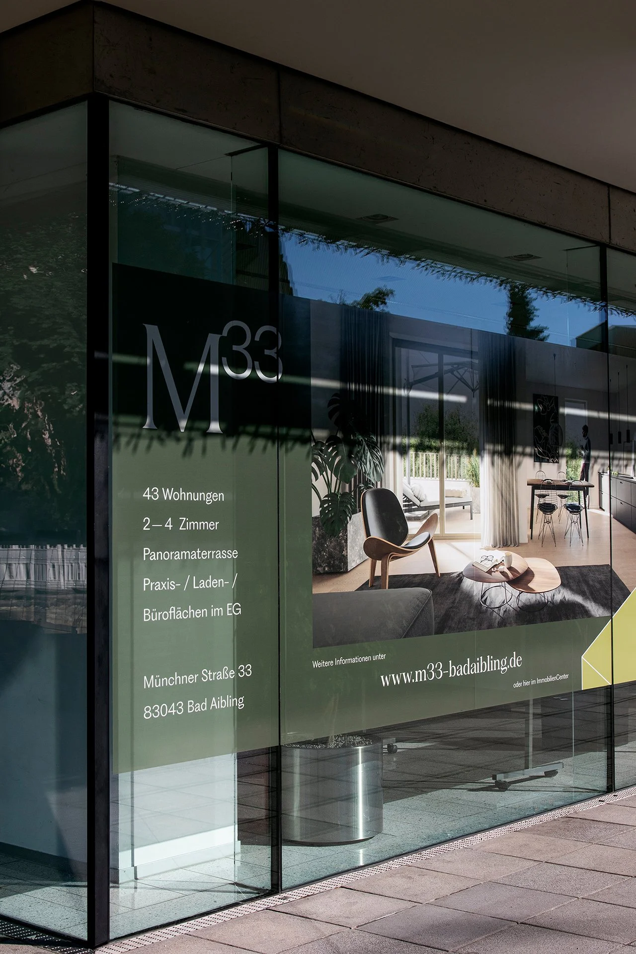 Fenster mit Informationen zu einer Wohnanlage, darunter Anzahl der Wohnungen, Zimmer, Dachterrasse, Praxis-, Laden- und Büroräume im Erdgeschoss, Adresse und Website.