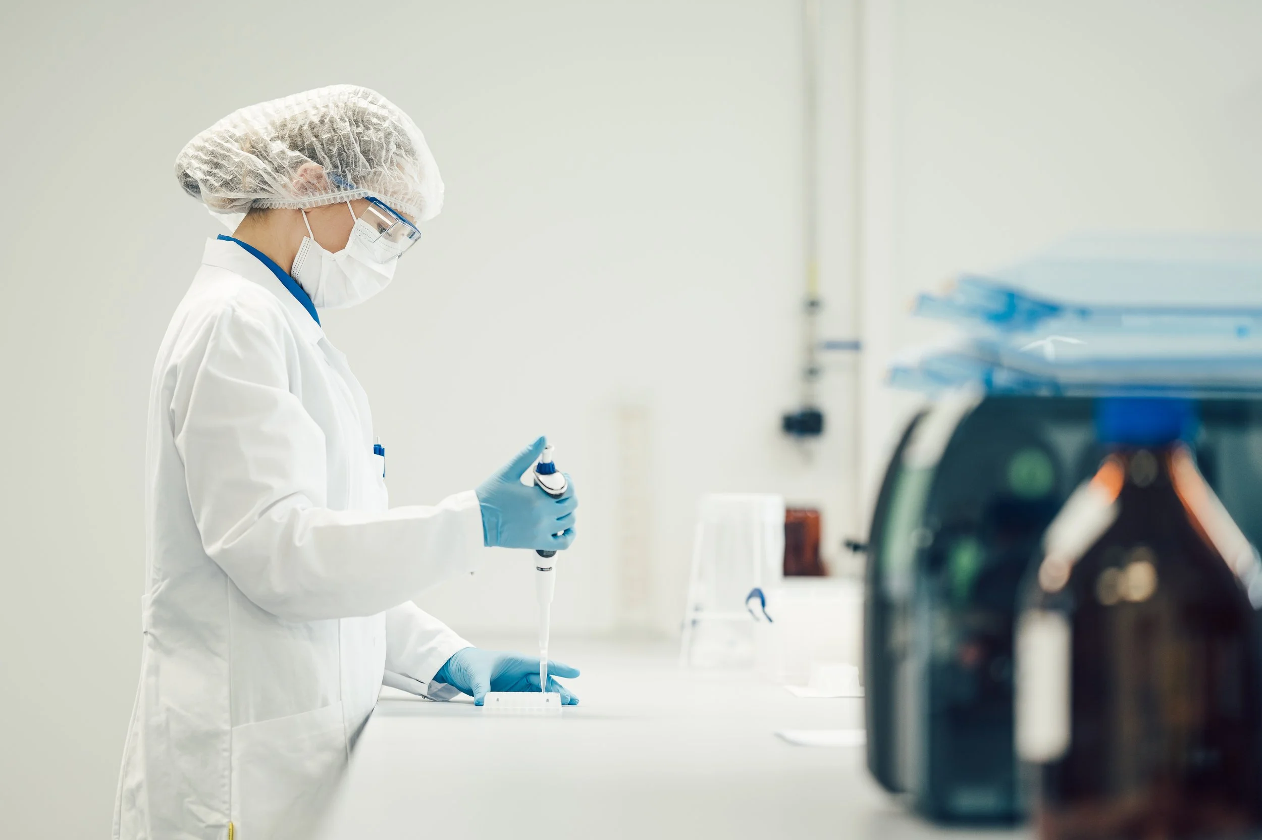 Ein Wissenschaftler oder Laborantin in Schutzkleidung, Maske, Schutzbrille und Handschuhen arbeitet im Labor und hält eine Pipette in der Hand.