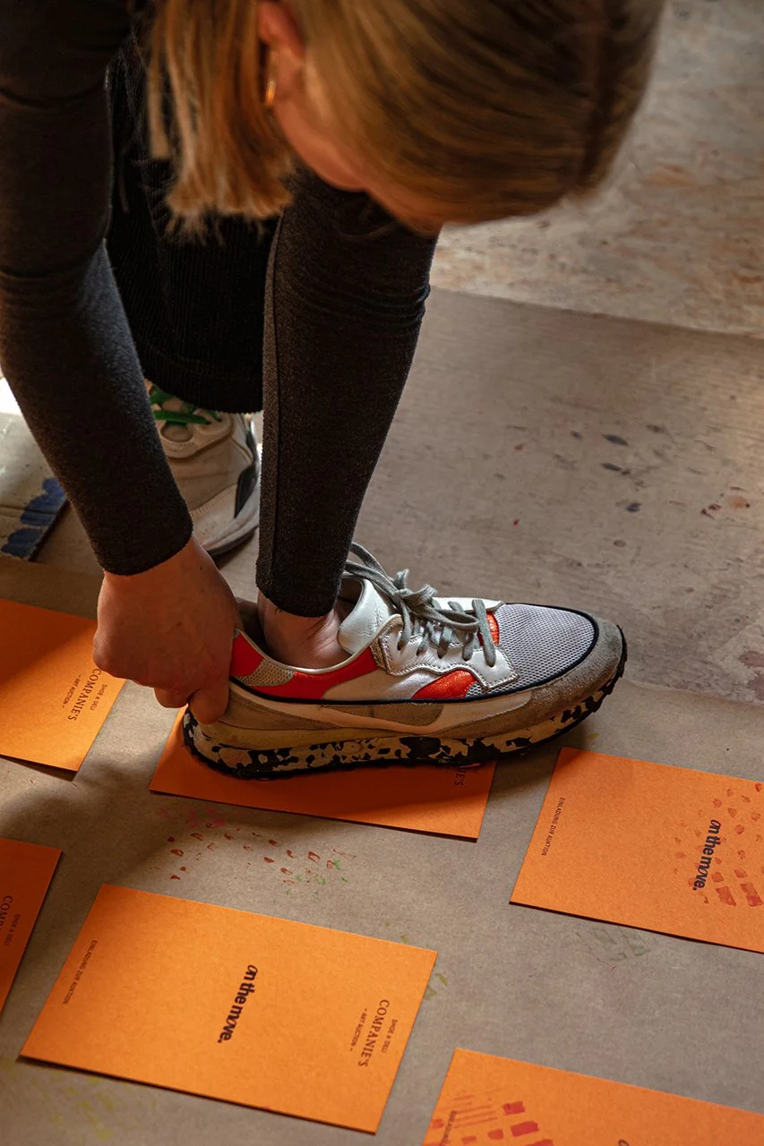 Person druckt mit einem Schuh auf orange Karten, die auf dem Boden liegen.
