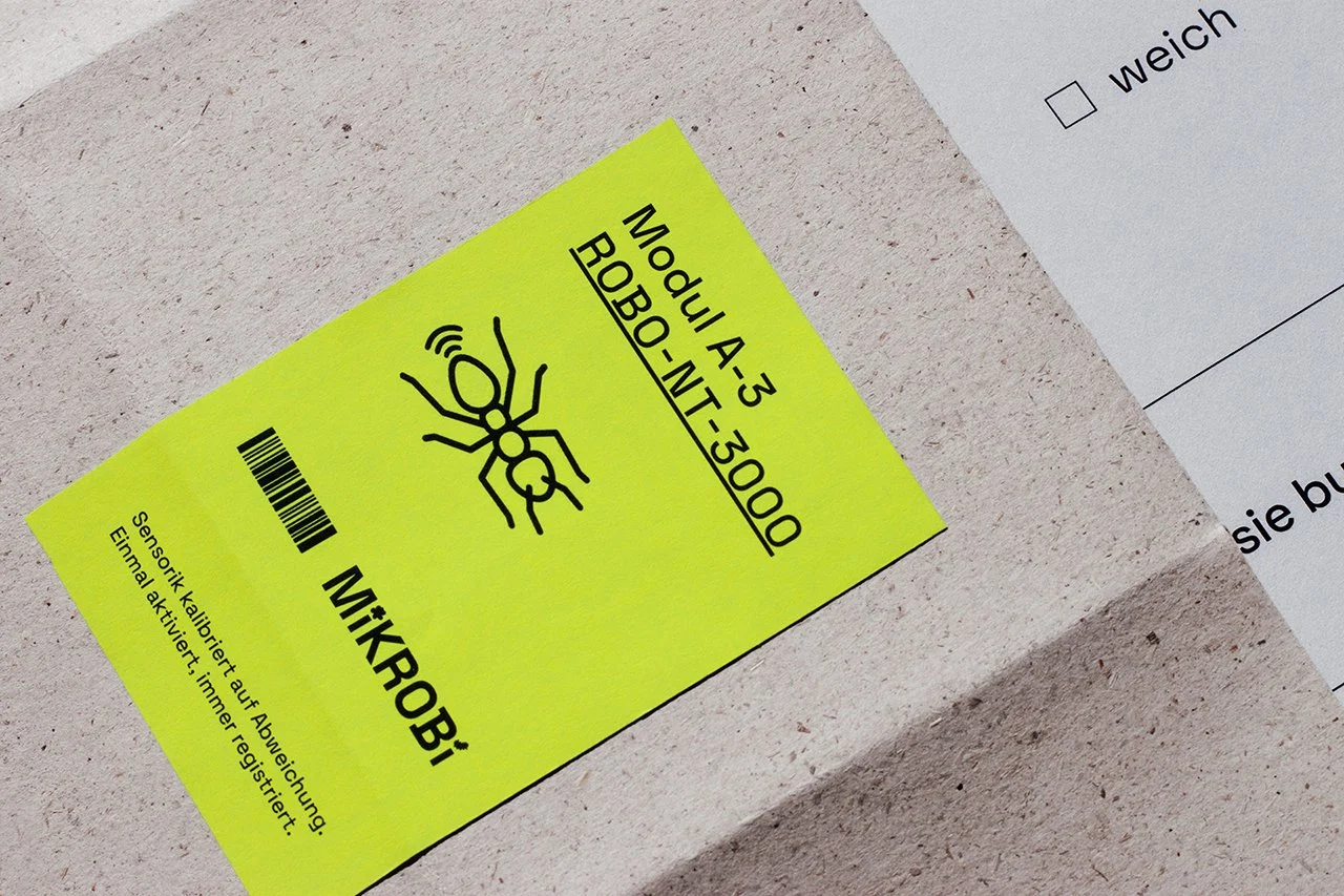 Gelbes Etikett mit einem Barcode, einer Antennenlinie, einem Käfer-Symbol und dem Text 'MikroBi'.