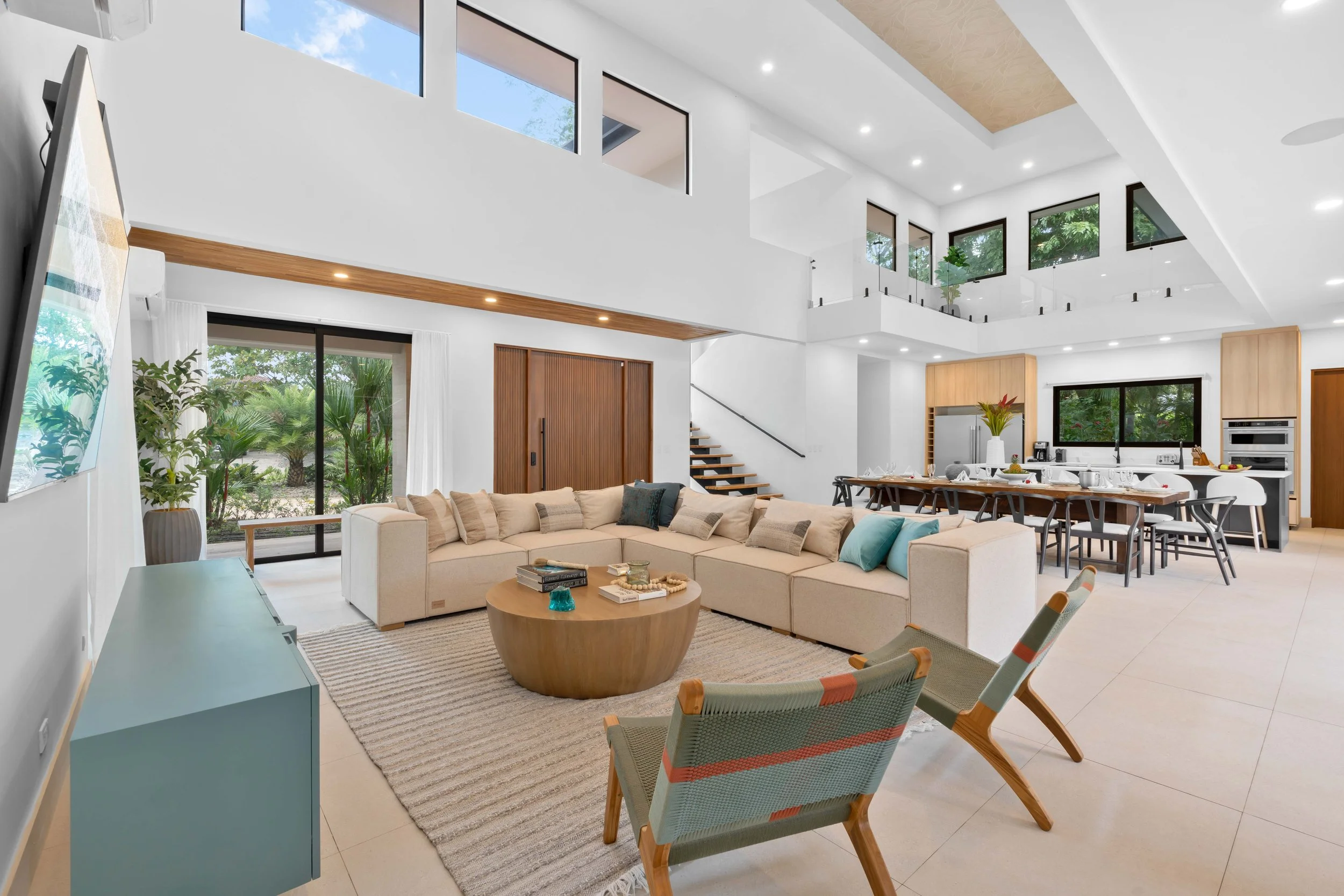 Open-concept living room and kitchen with modern furniture, large windows, and indoor plants.