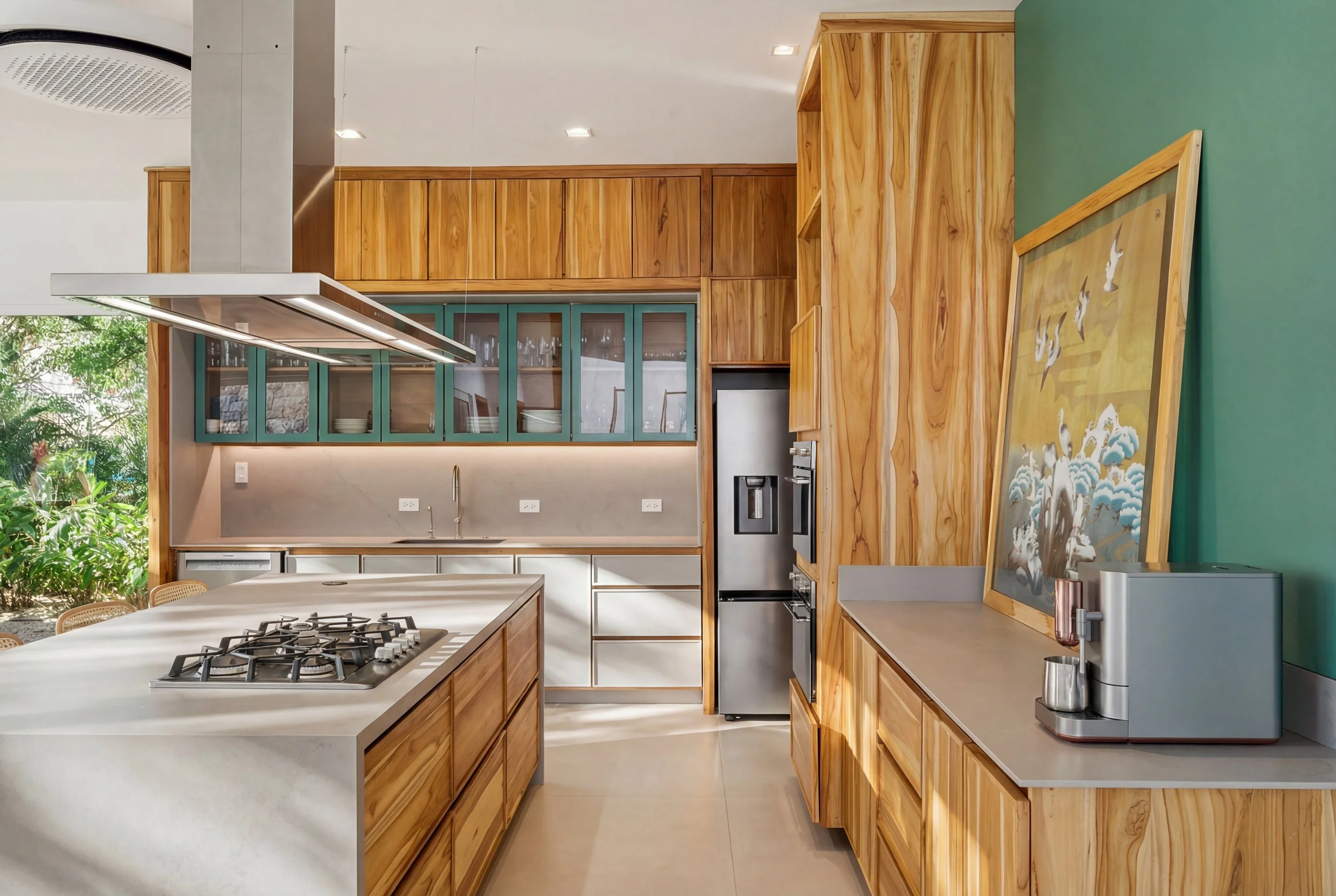 Modern kitchen with wooden cabinets, a large island with a gas stove, stainless steel refrigerator, green upper cabinets, and bright natural light.
