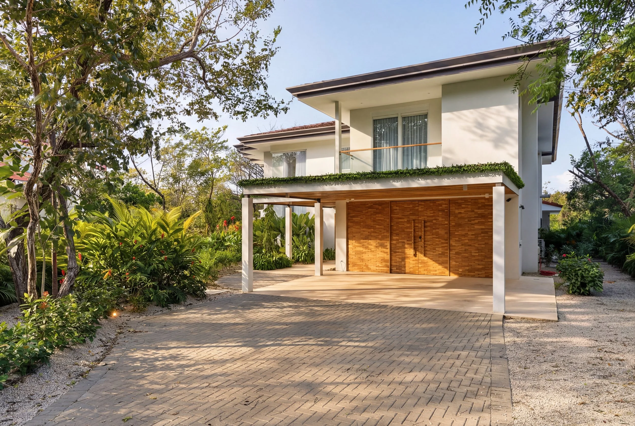 Modern two-story house with a large driveway, wooden garage doors, and lush greenery surrounding the property. In Guanacaste, Costa Rica. 