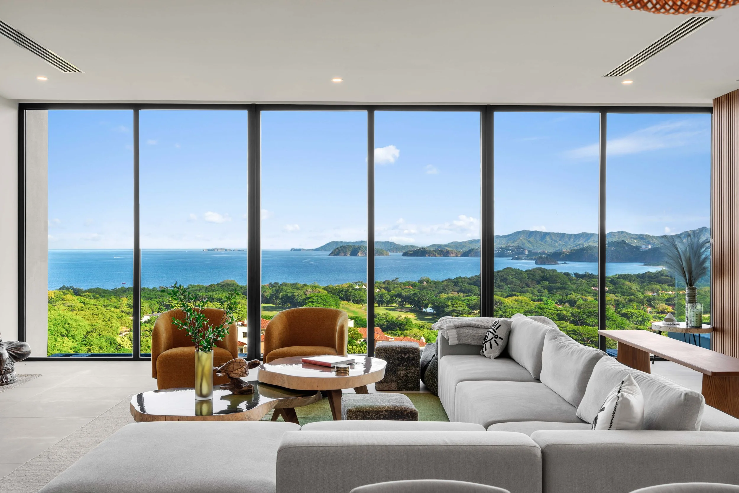 Interior of a modern living room with large floor-to-ceiling windows overlooking a lush green landscape, water, and islands in the distance.