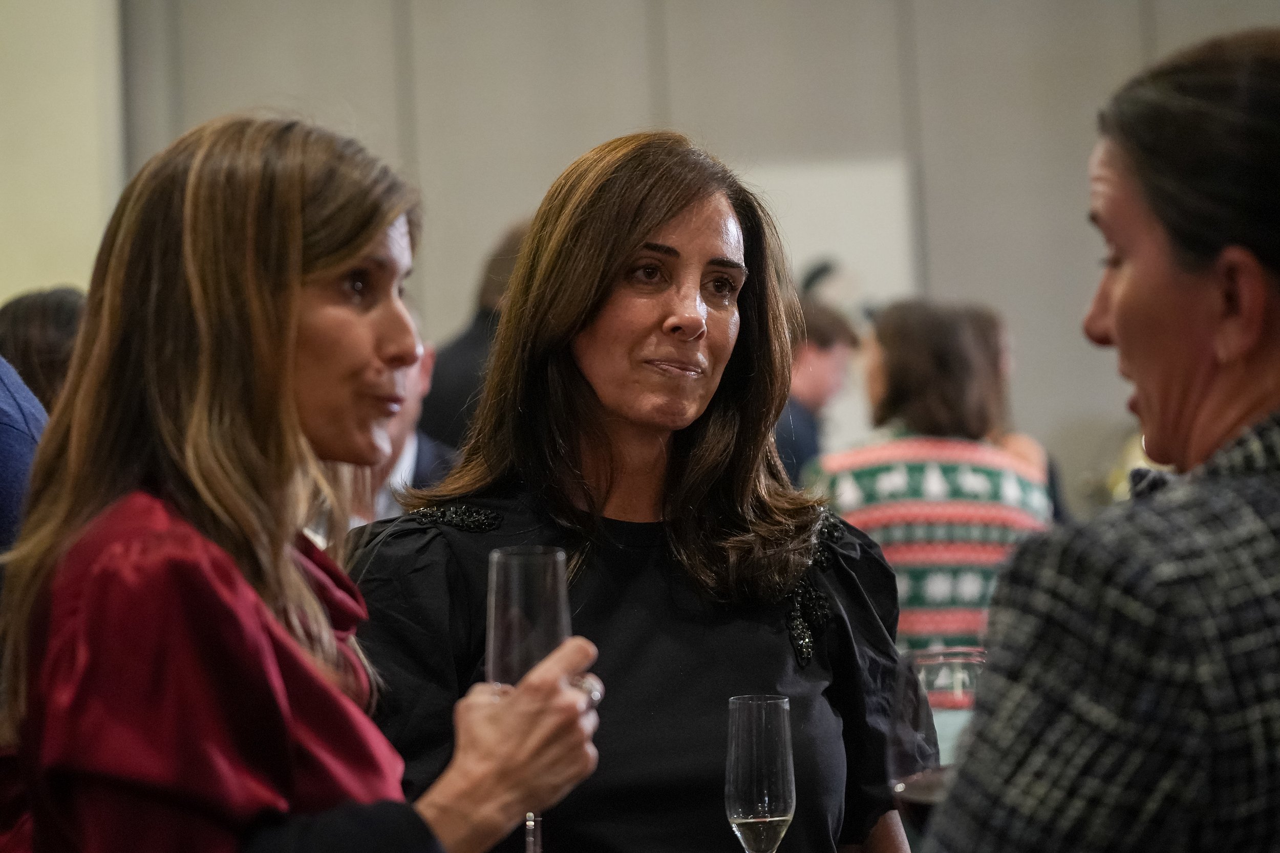 Three women engaged in conversation at an event, holding glasses of champagne.