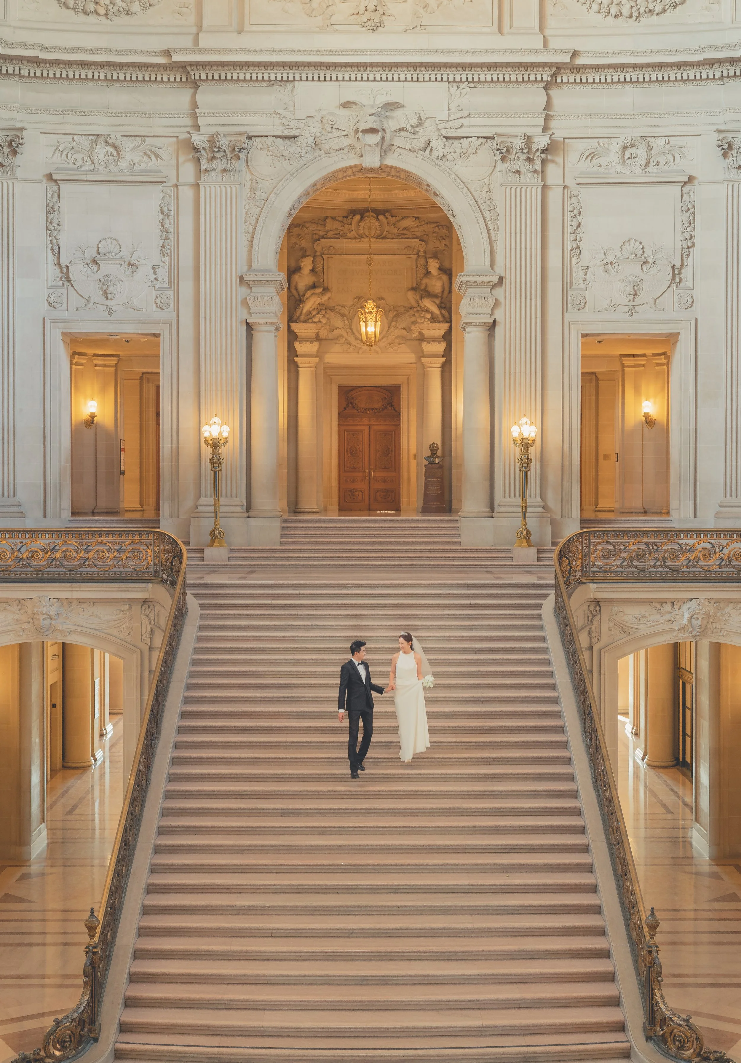 Couple standing on the grand staircase inside San Francisco City Hall, surrounded by elegant marble architecture.