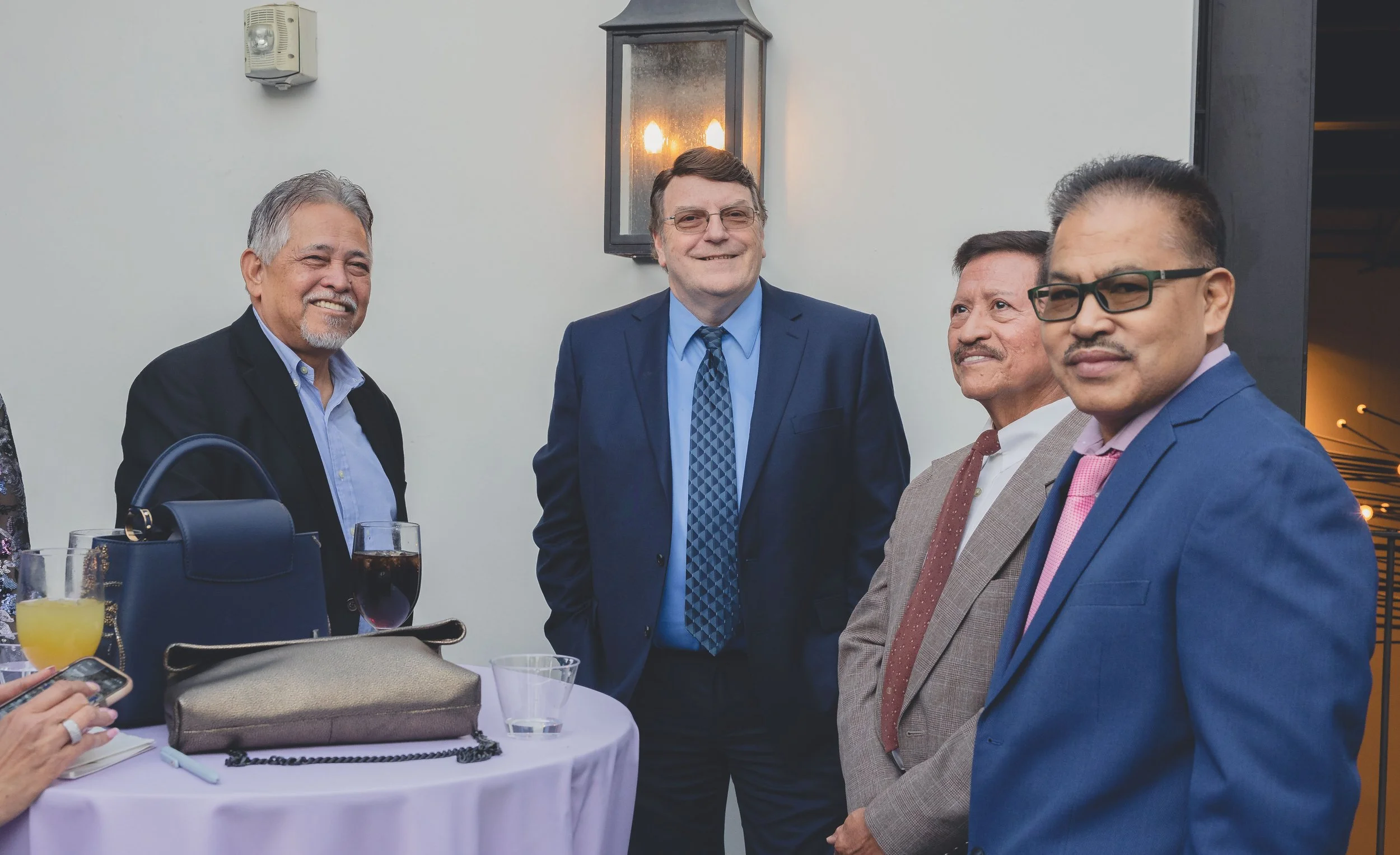 Group of men in formal attire socializing near a lit wall sconce.