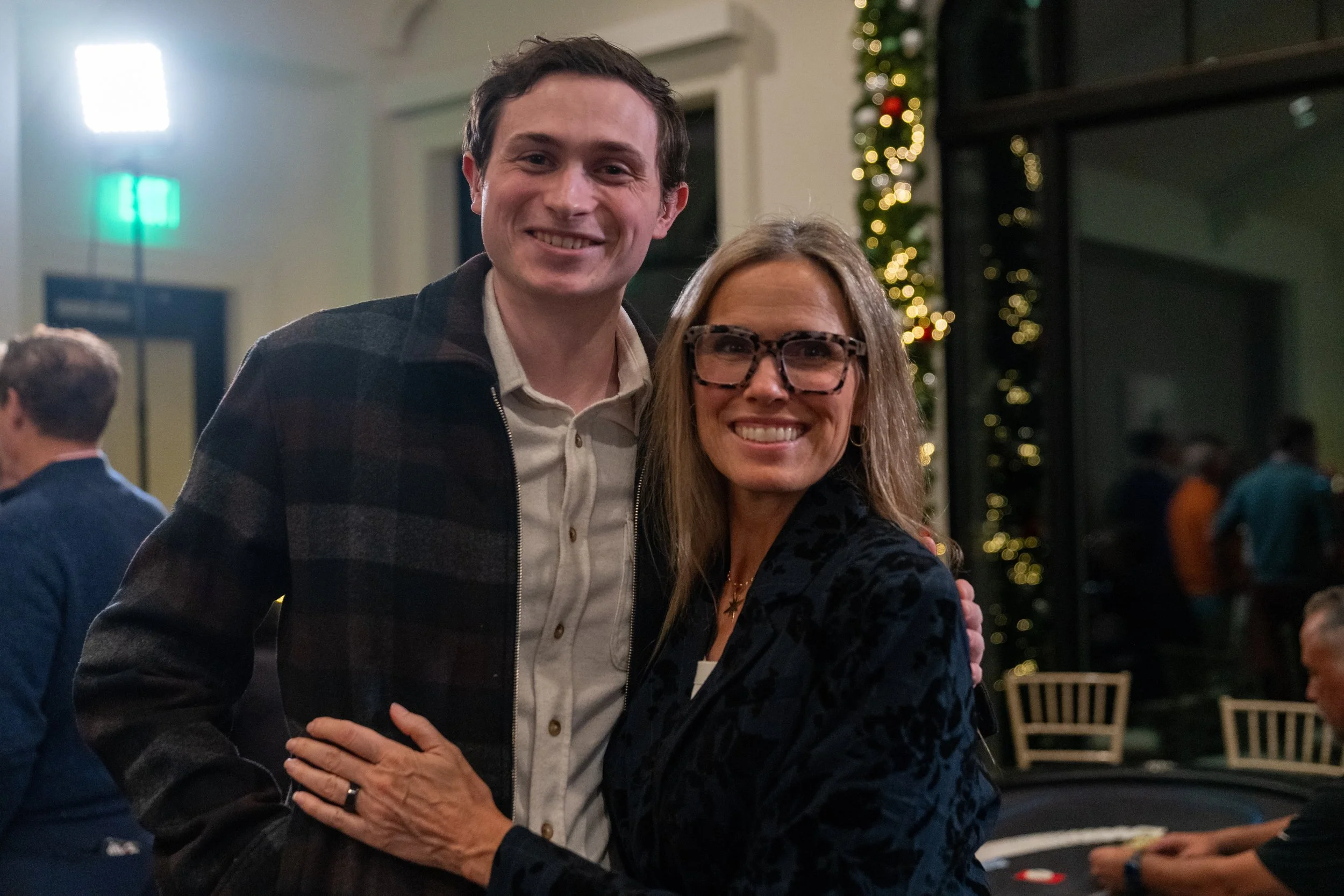 Two people smiling indoors with holiday decorations in the background.