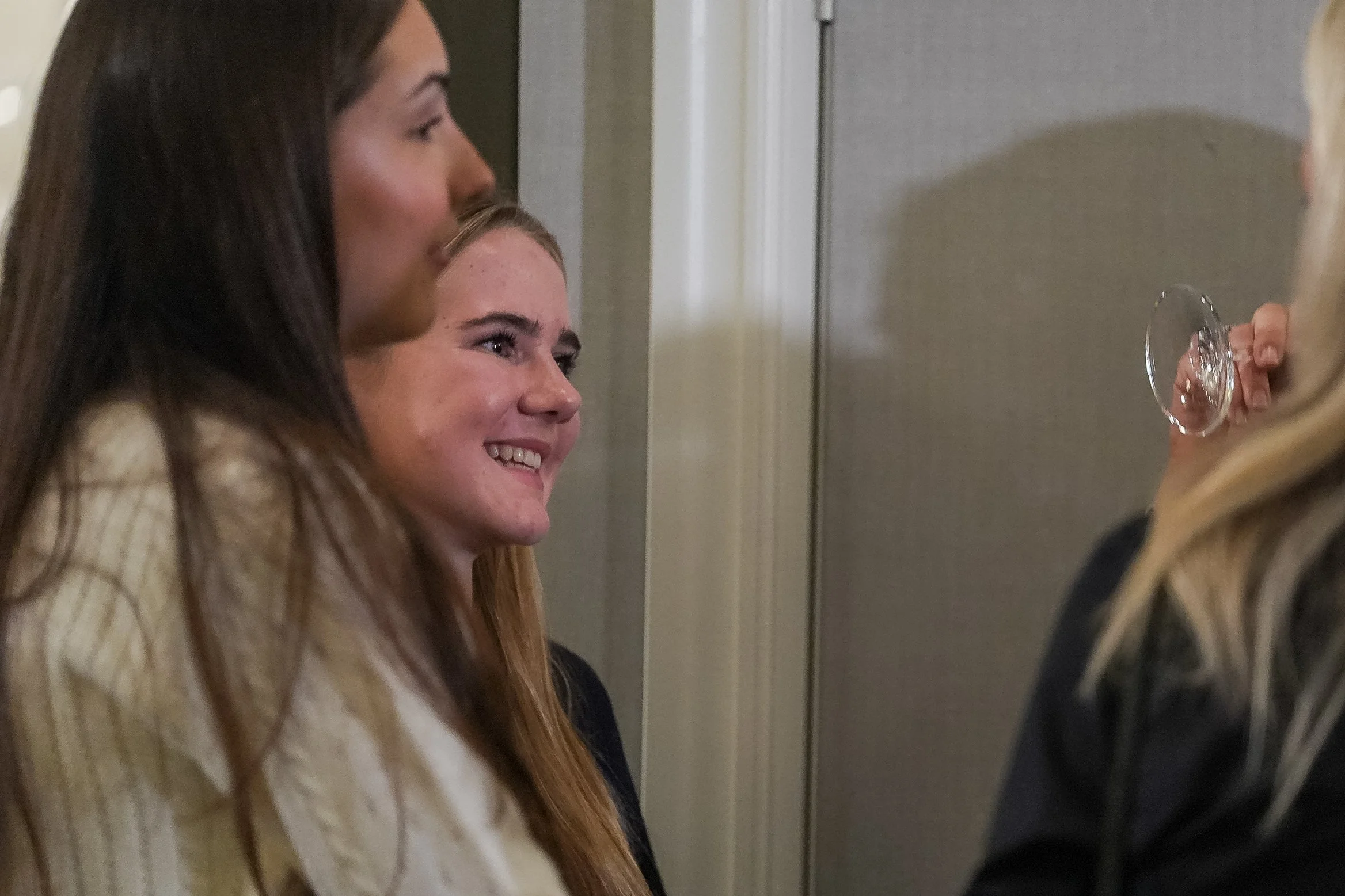 Group of people talking and smiling, one holding an empty wine glass in a social setting.