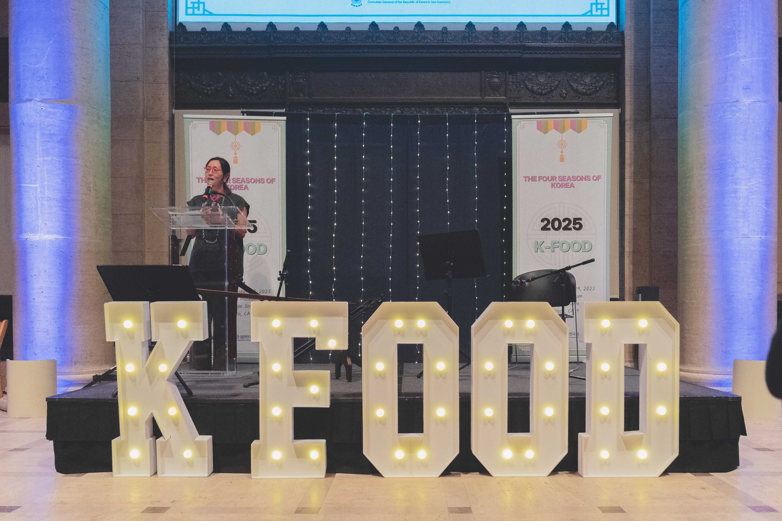A woman giving a speech on a stage with large illuminated letters spelling 