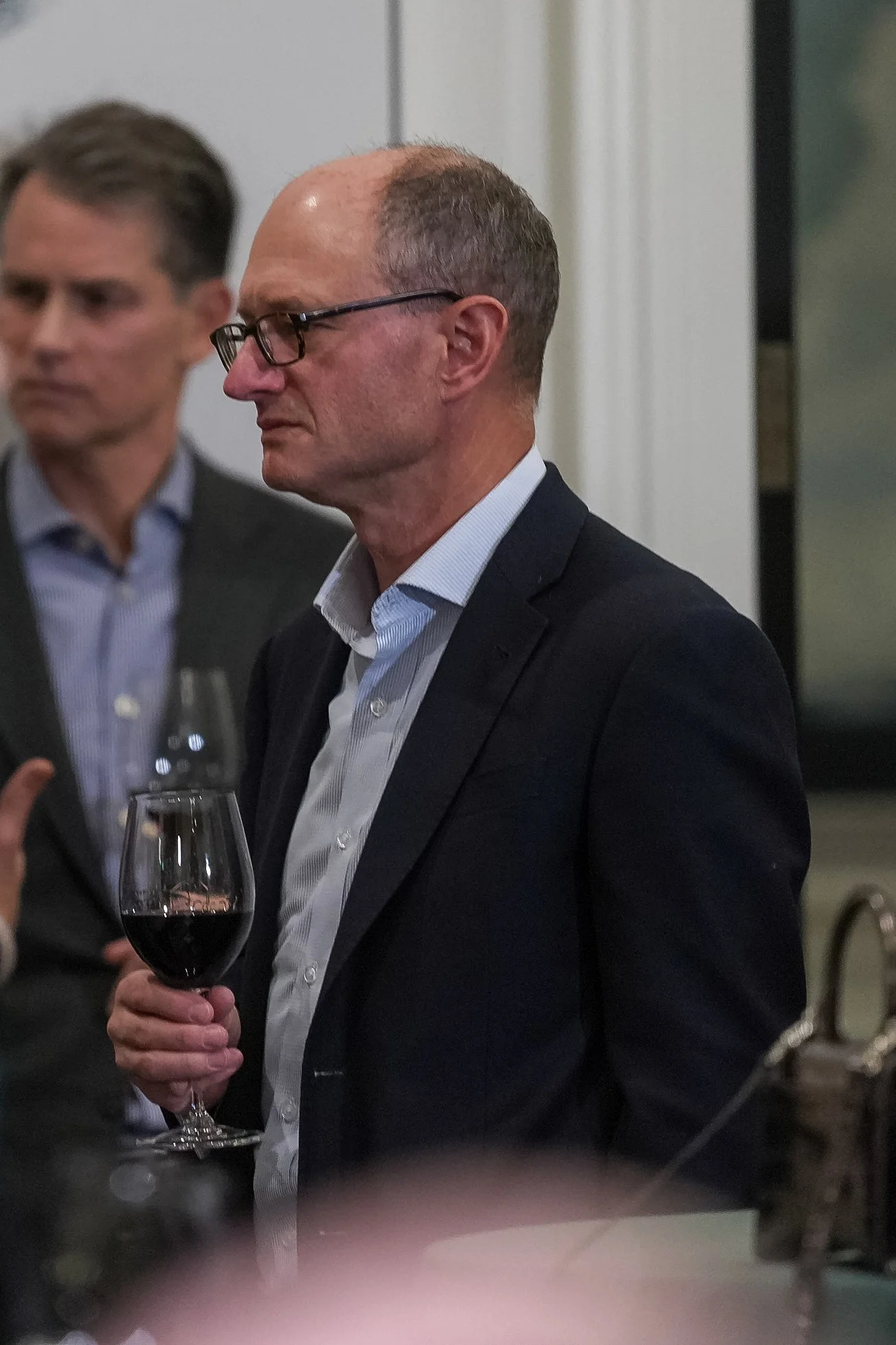 Man in a suit holding a glass of red wine at an event.