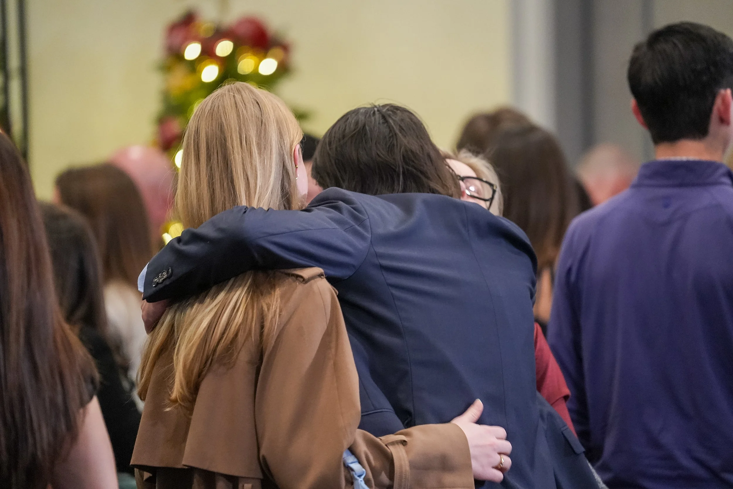 Group of people hugging at an event with blurred festive lights in the background.