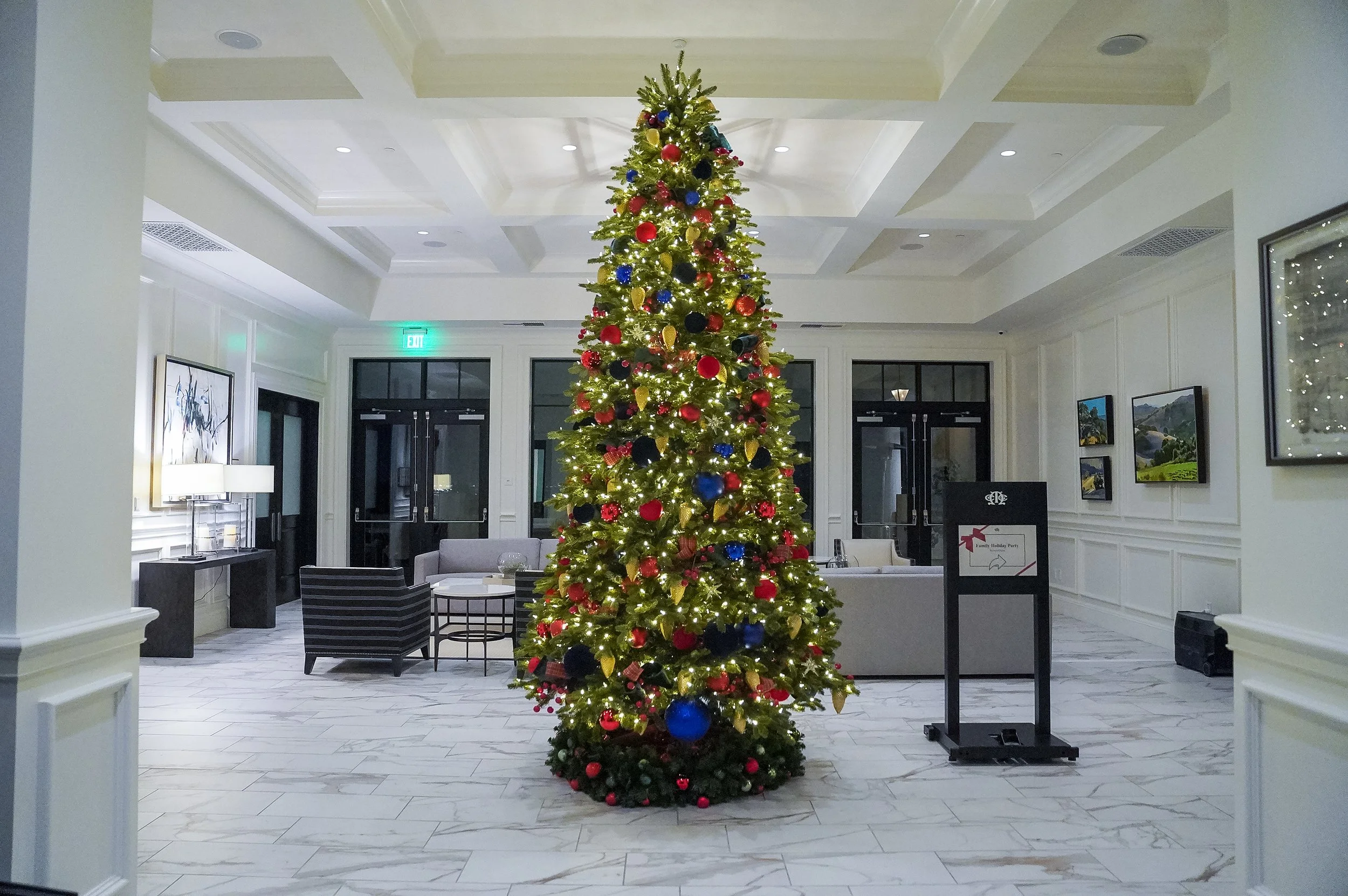 Decorated Christmas tree in a hotel lobby with marble flooring and modern furniture.